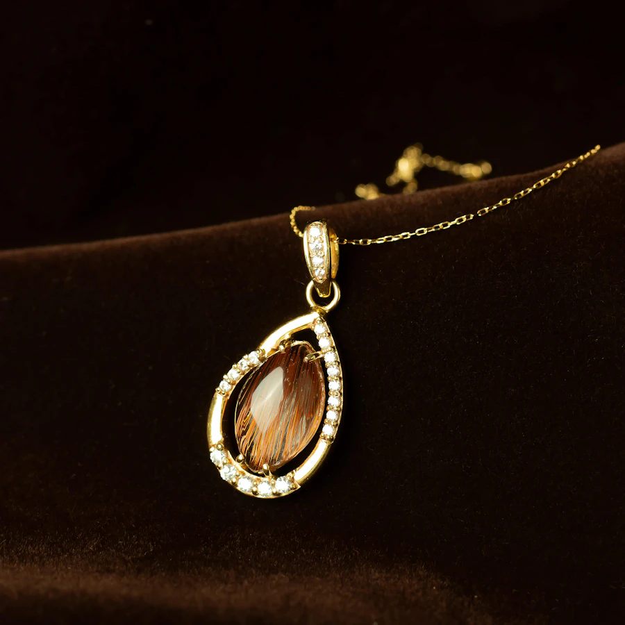 A gold teardrop pendant set with a golden stone, on dark velvet