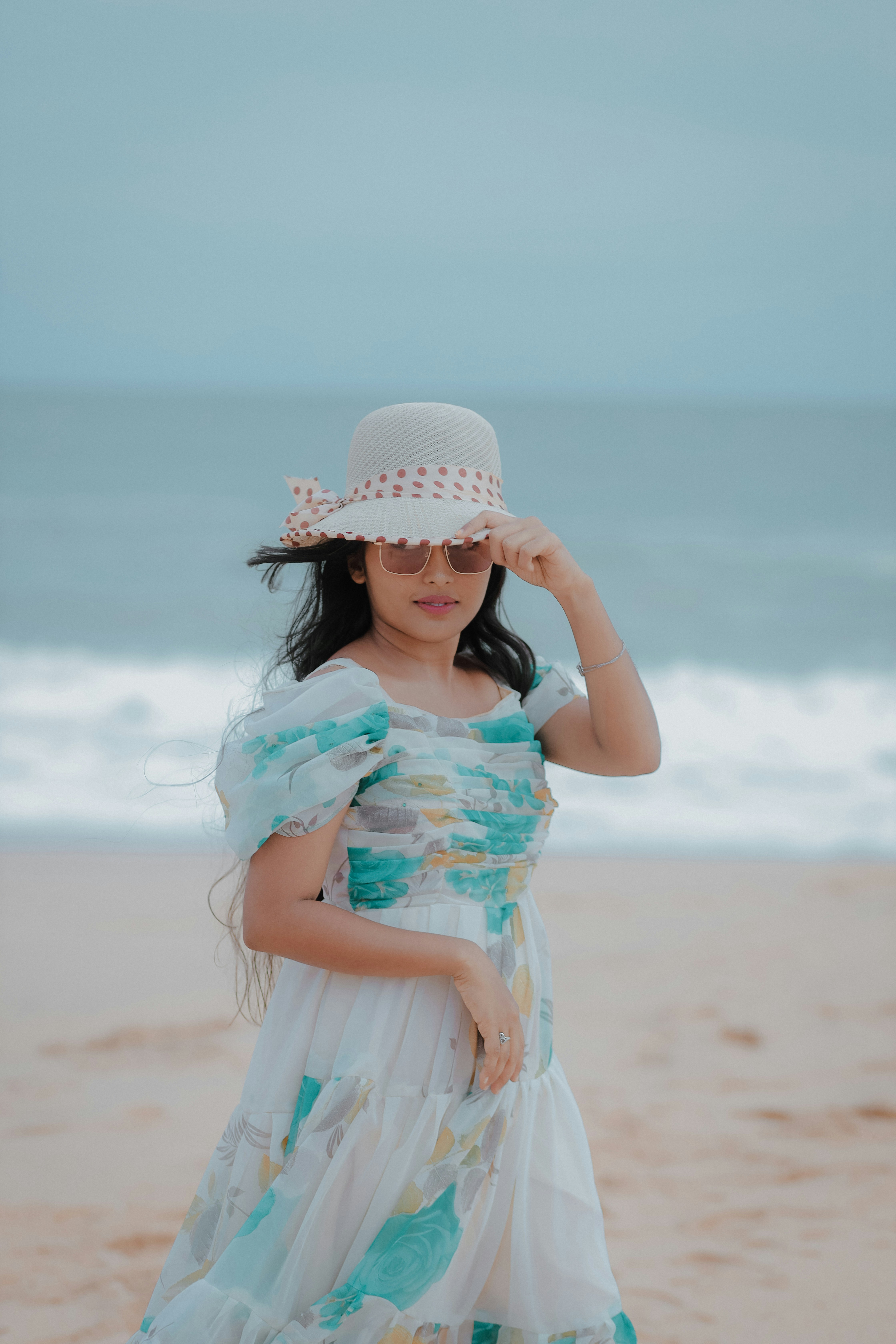 A little girl in a dress and hat on the beach
