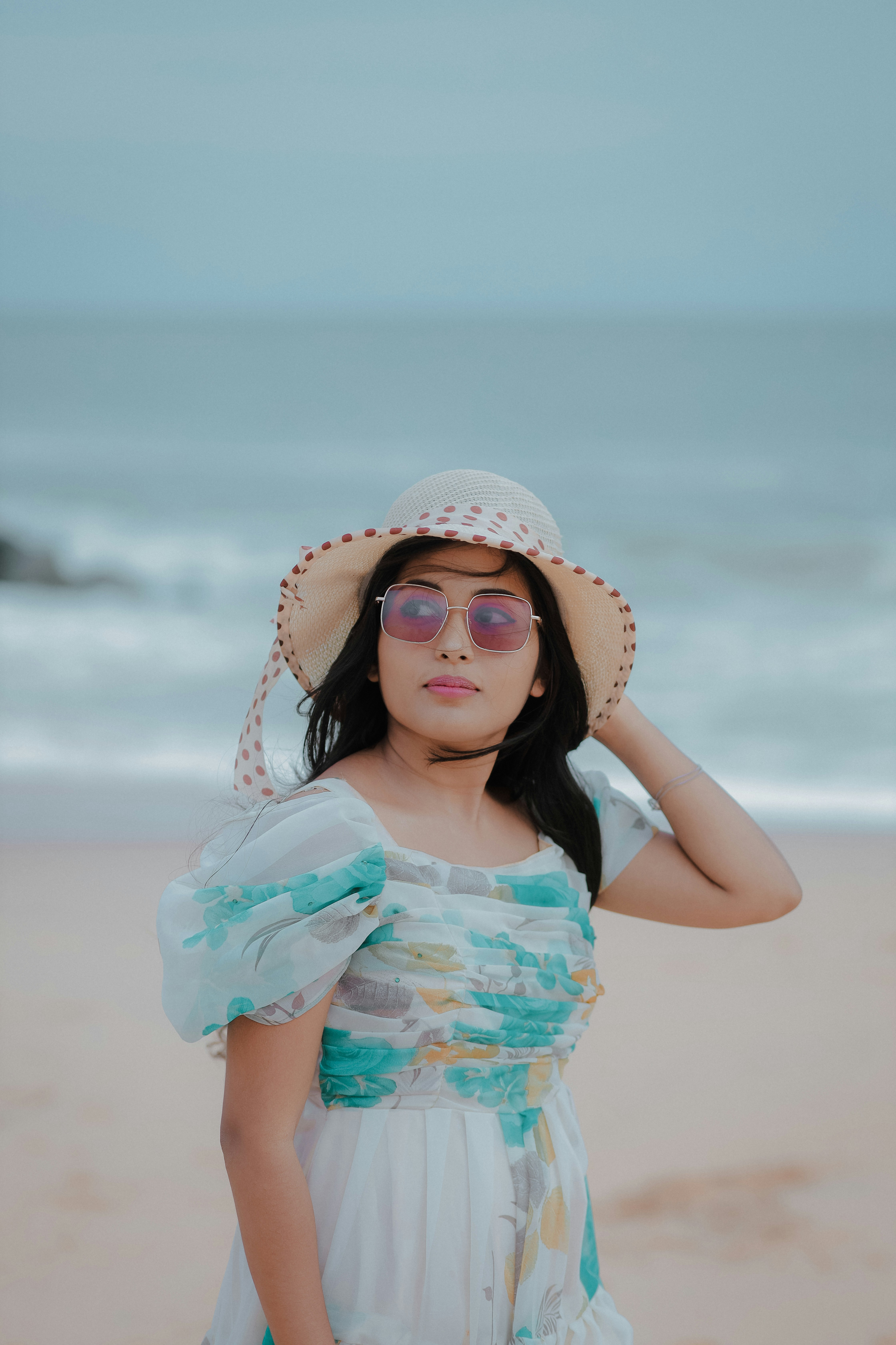 A woman in a dress and hat on the beach