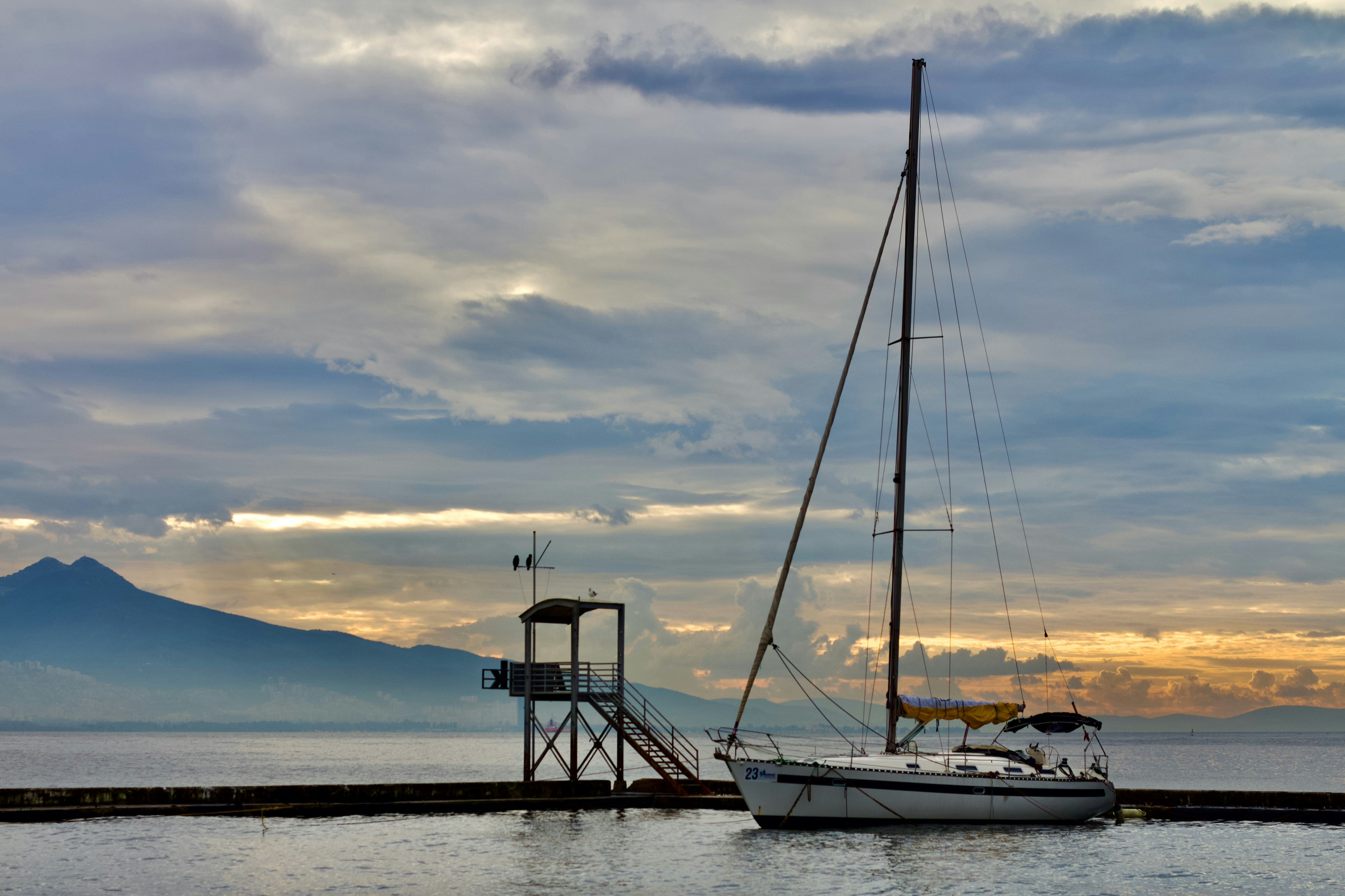 A sailboat is docked at a pier with a mountain in the background