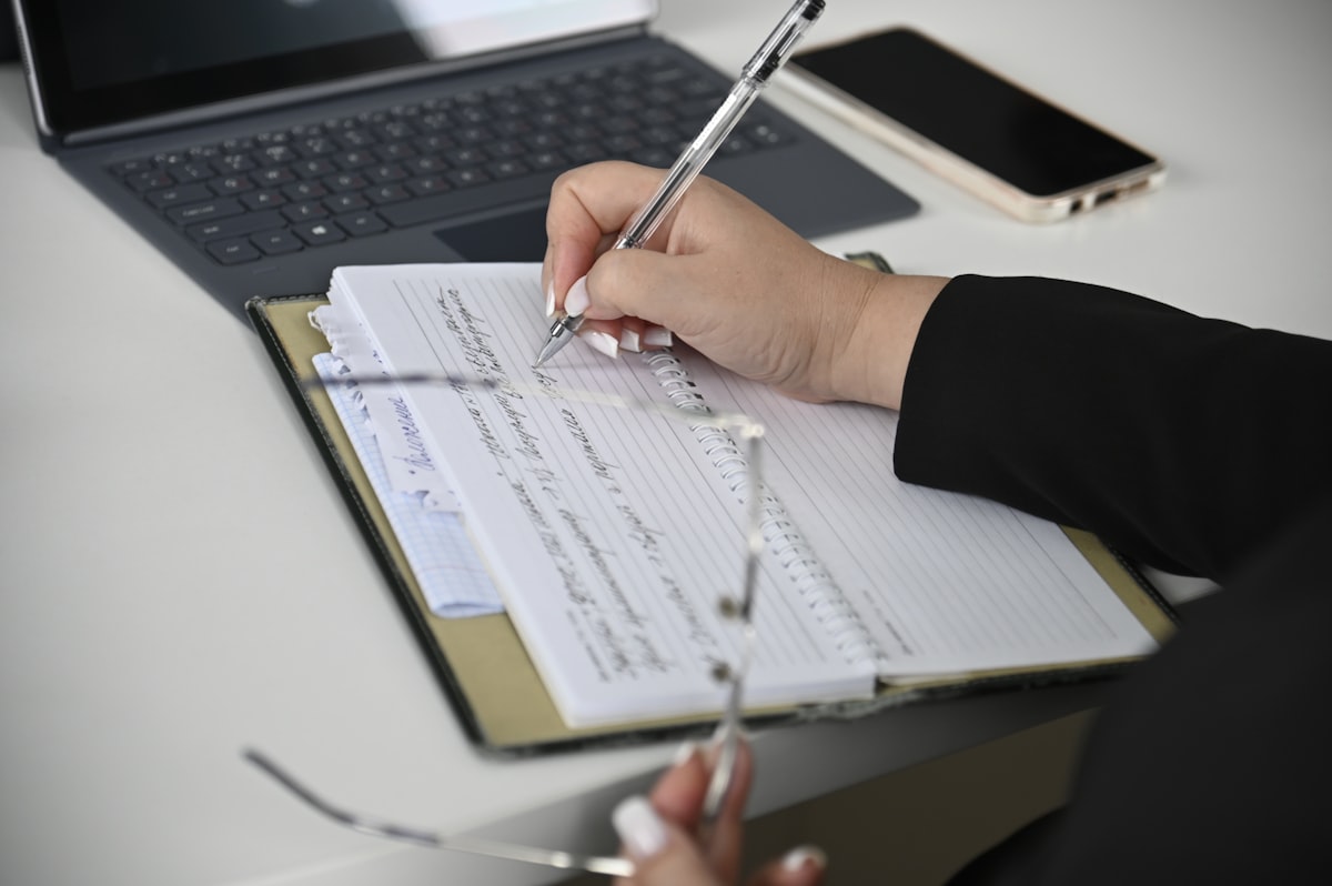 Person writing in a notebook with a laptop open in the background, representing the process of turning customer research into landing page copy