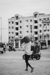 A man walking across a street carrying a bucket on his head