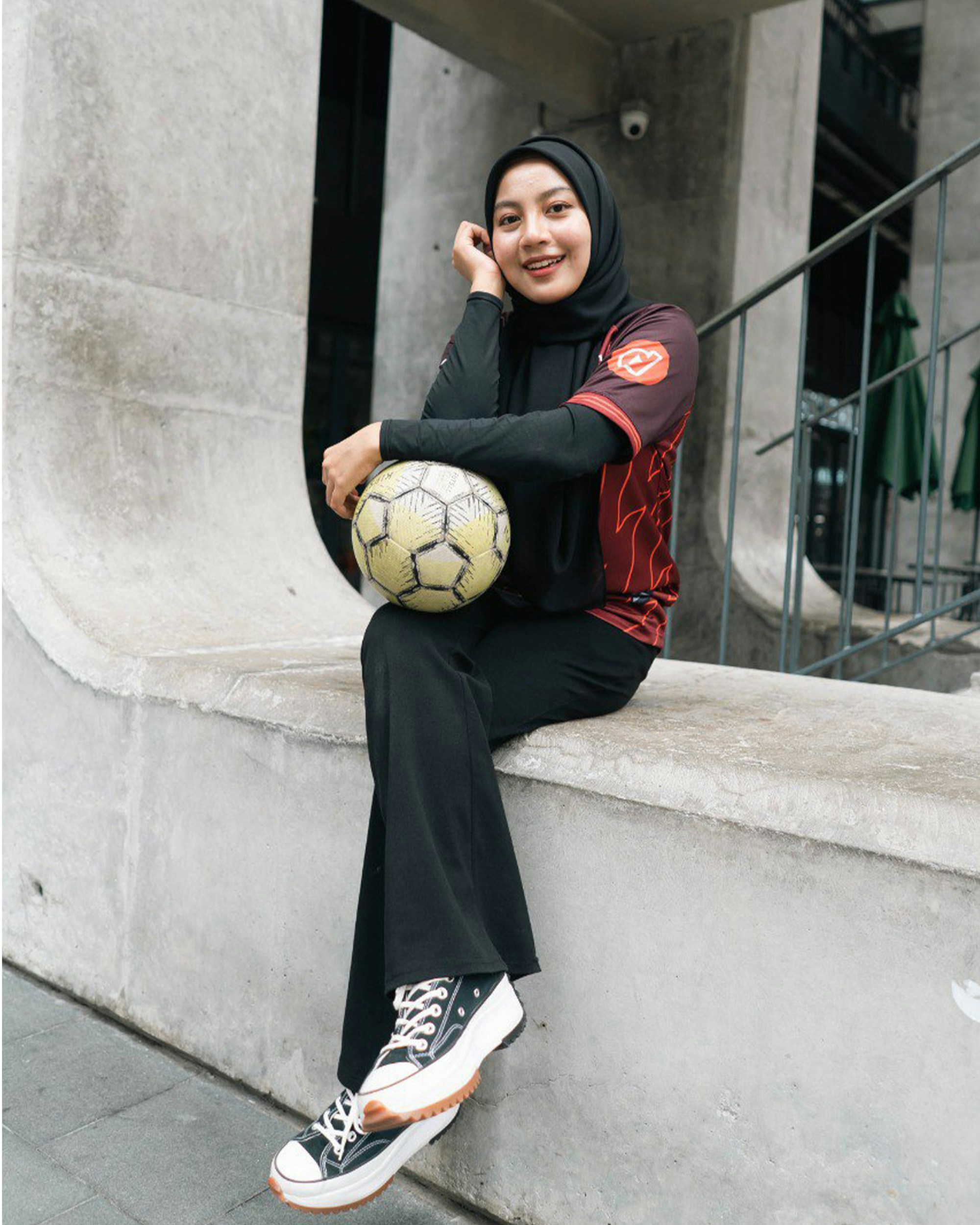 Seorang wanita duduk di langkan dengan bola sepak