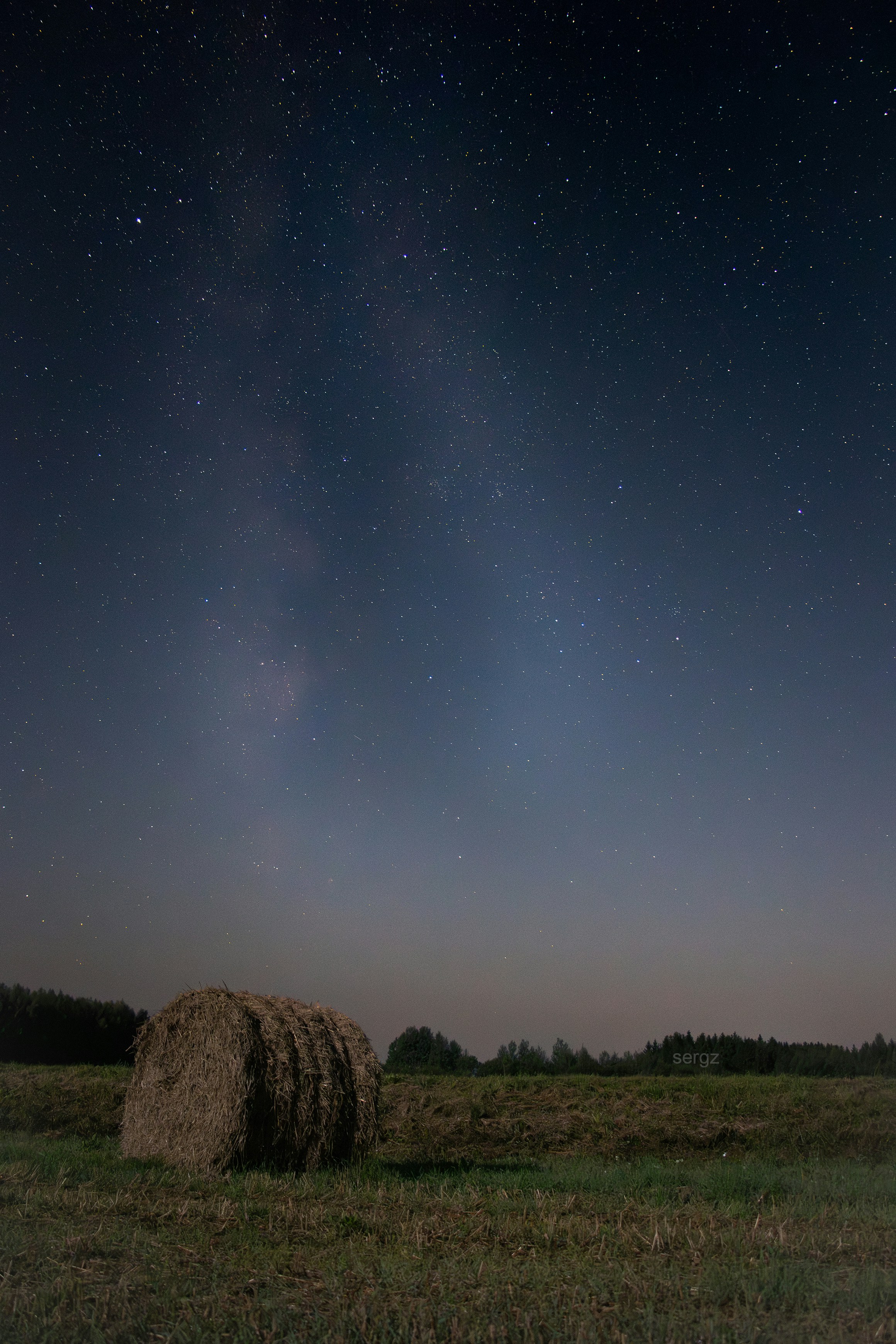 A hay bale sitting in a field under a night sky