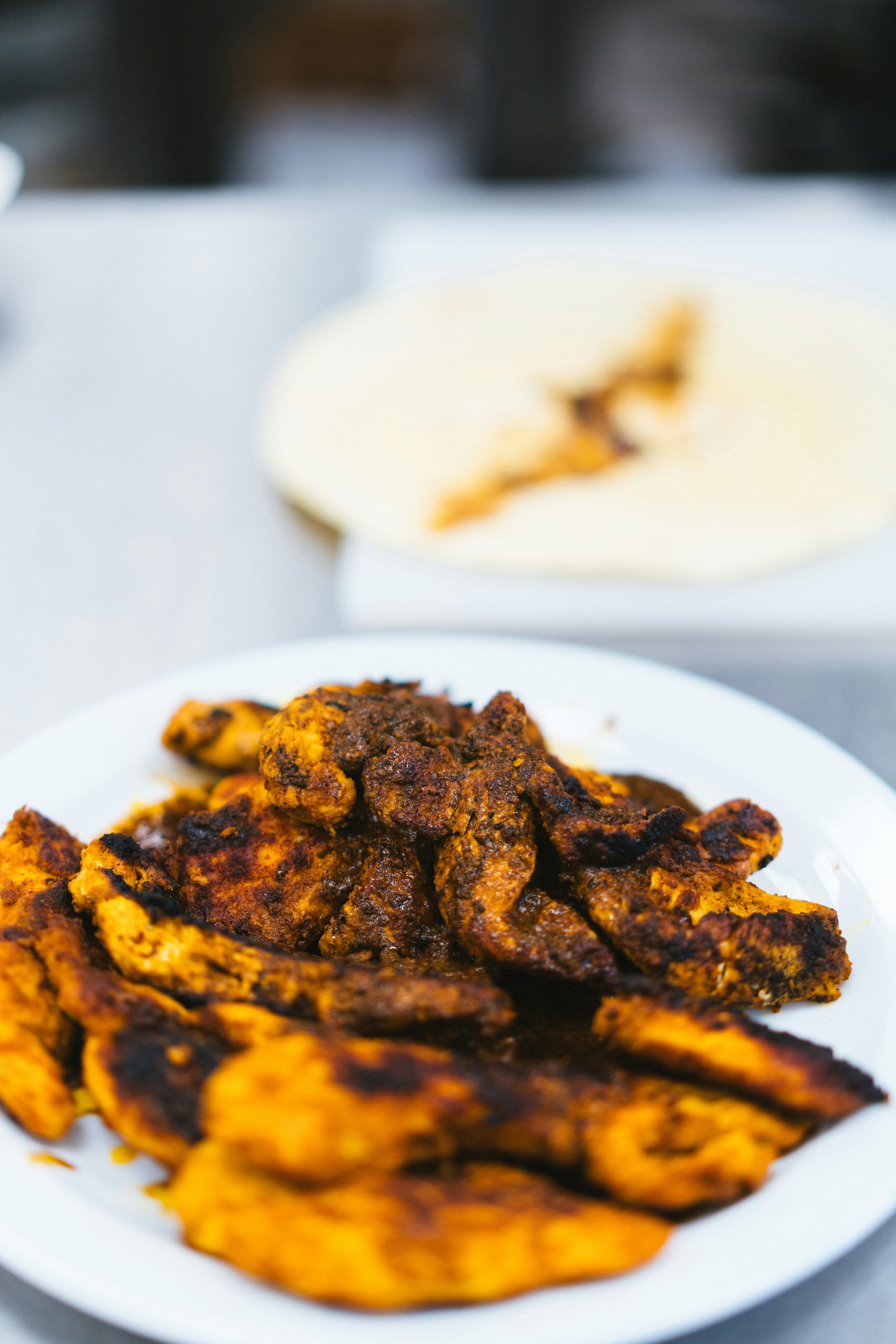 Charred, spice-marinated chicken pieces on a white plate, with a flatbread behind
