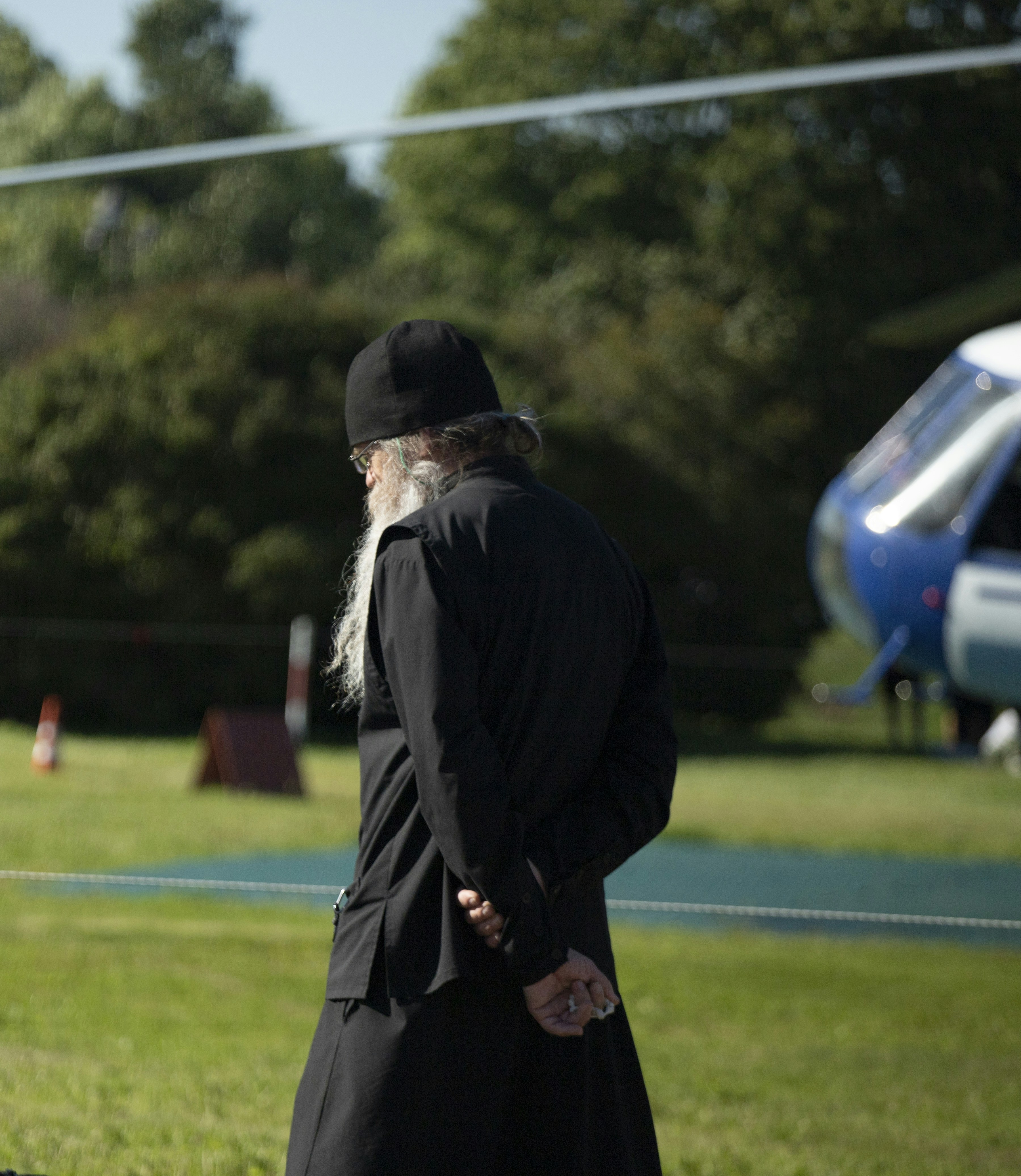 A man with a long white beard standing in a field next to a helicopter