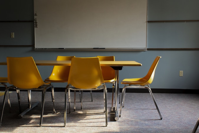 A bright classroom with a whiteboard and rows of empty yellow chairs waiting for students
