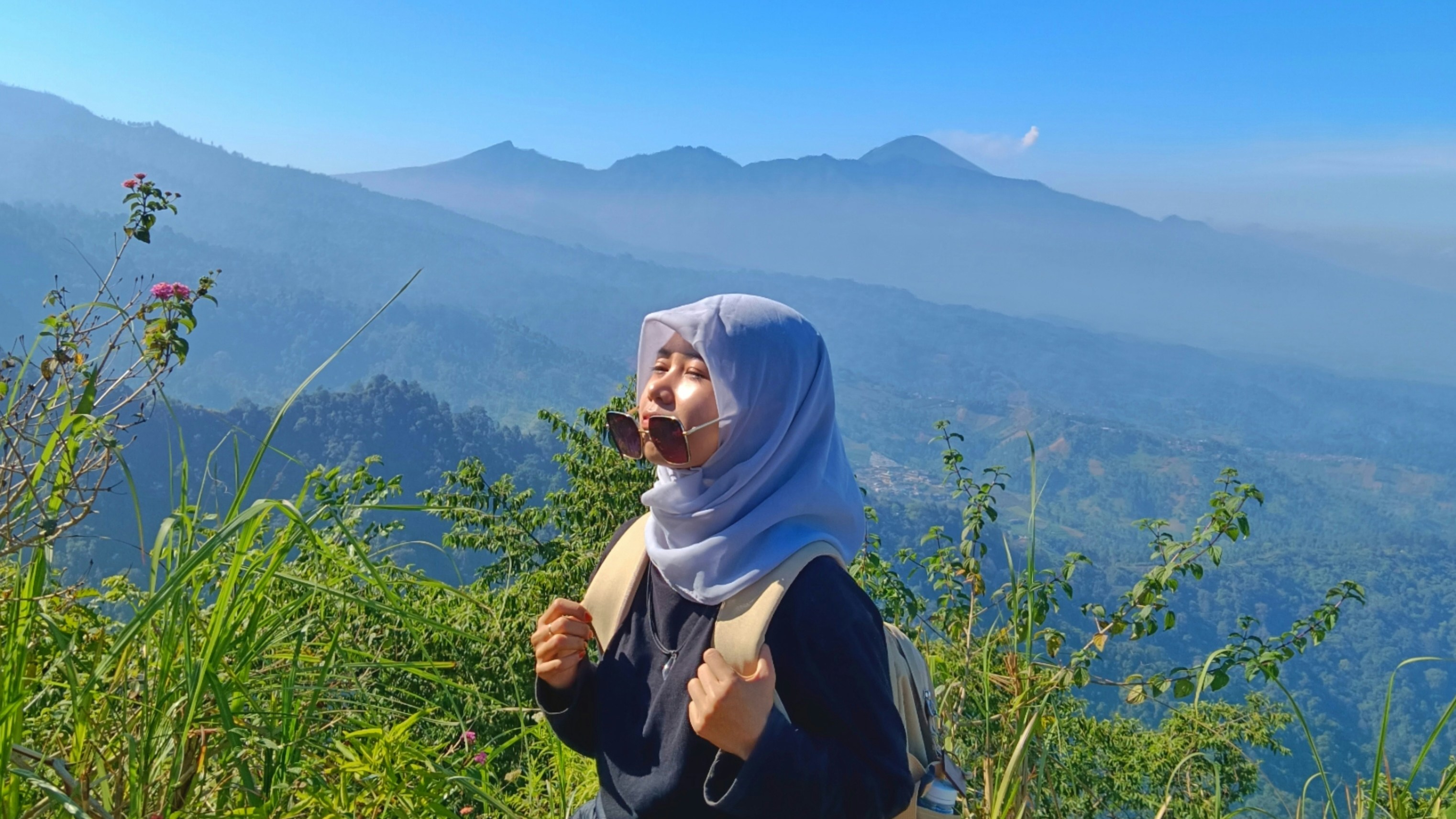 Seorang wanita berdiri di atas lereng bukit hijau subur