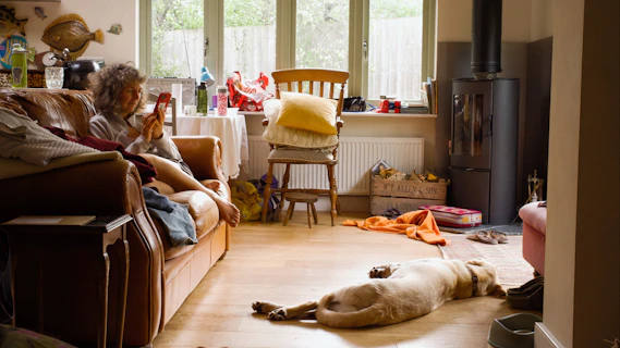 A woman on a sofa and a dog laying on the floor in a living room in a messy room