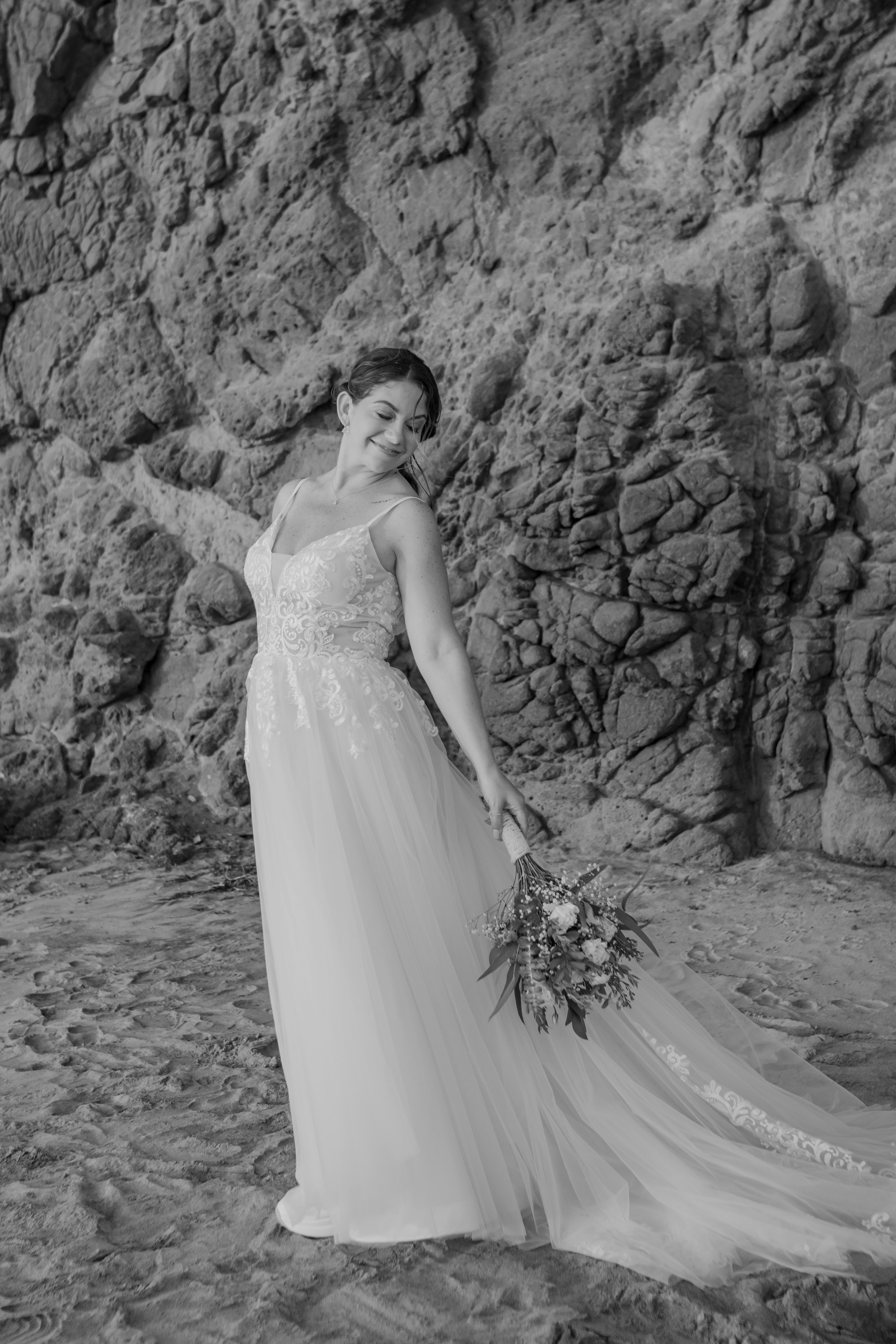 A woman in a wedding dress standing in front of a rock wall