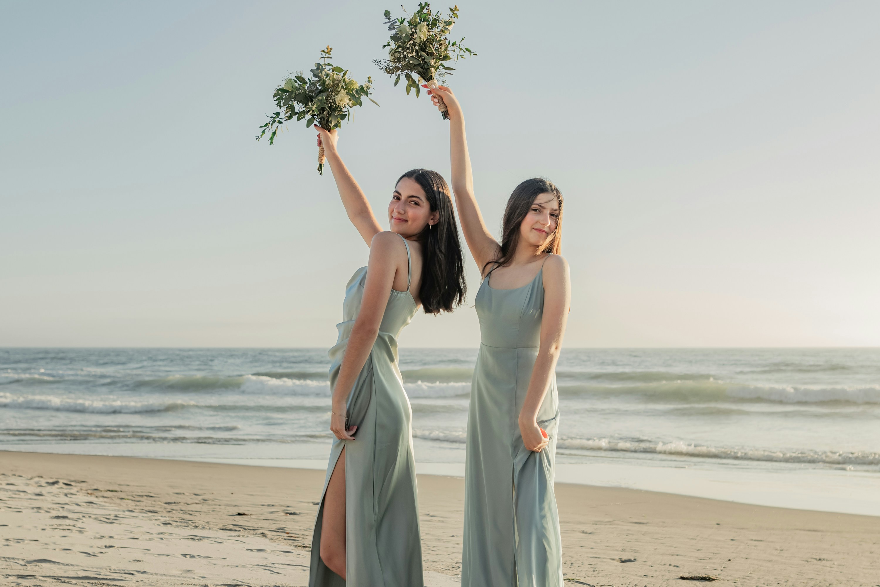 Two beautiful women standing on top of a sandy beach
