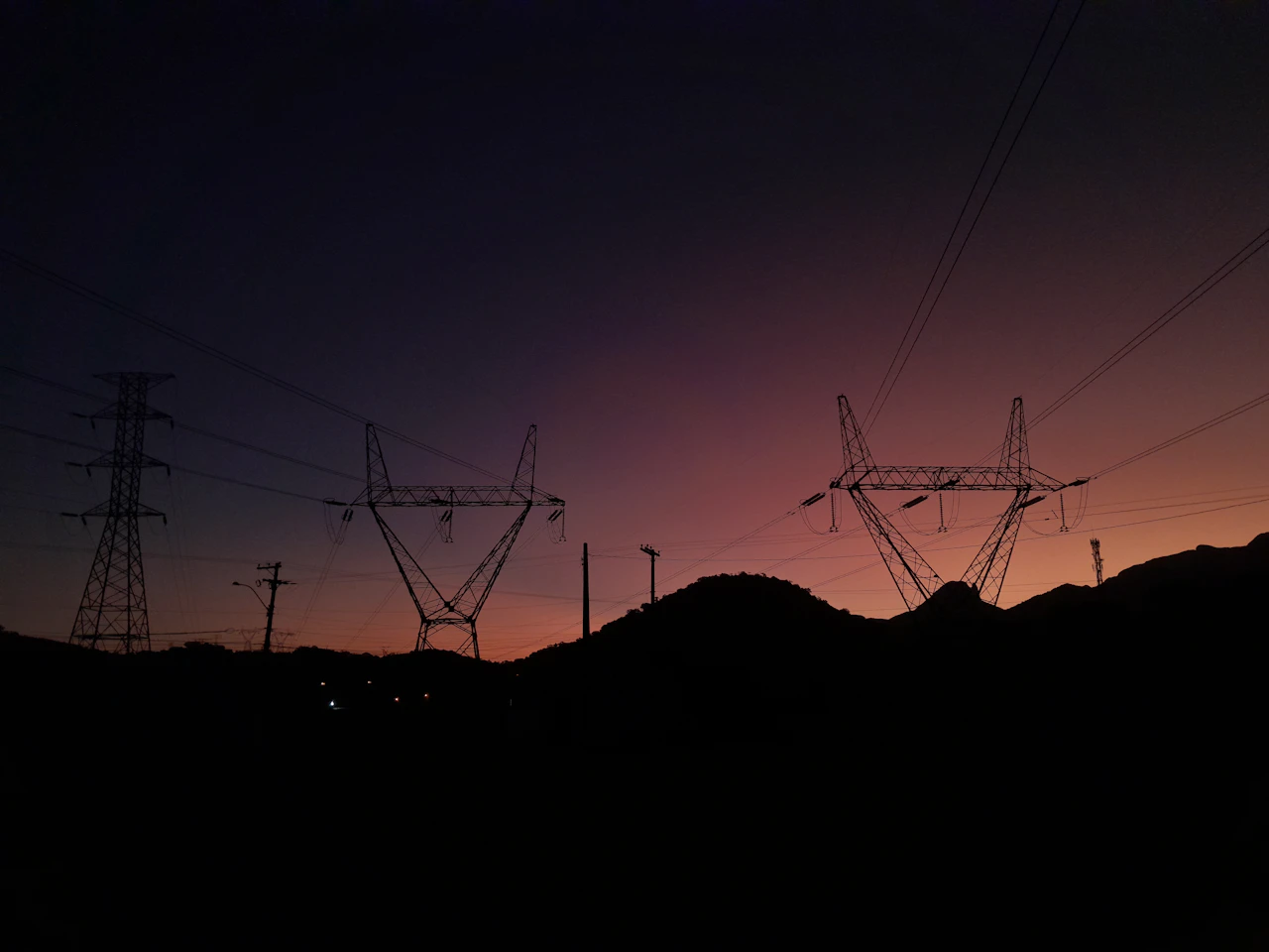 Transmission towers silhouetted against a mountain sunset