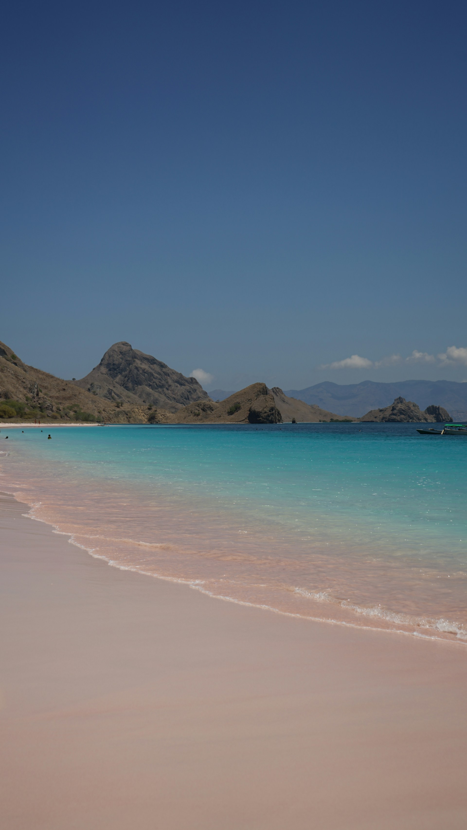 A sandy beach with clear blue water and mountains in the background