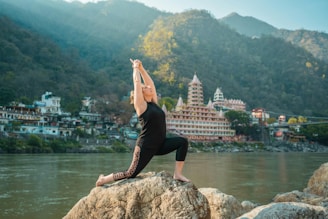 A woman is doing yoga on a rock by the water