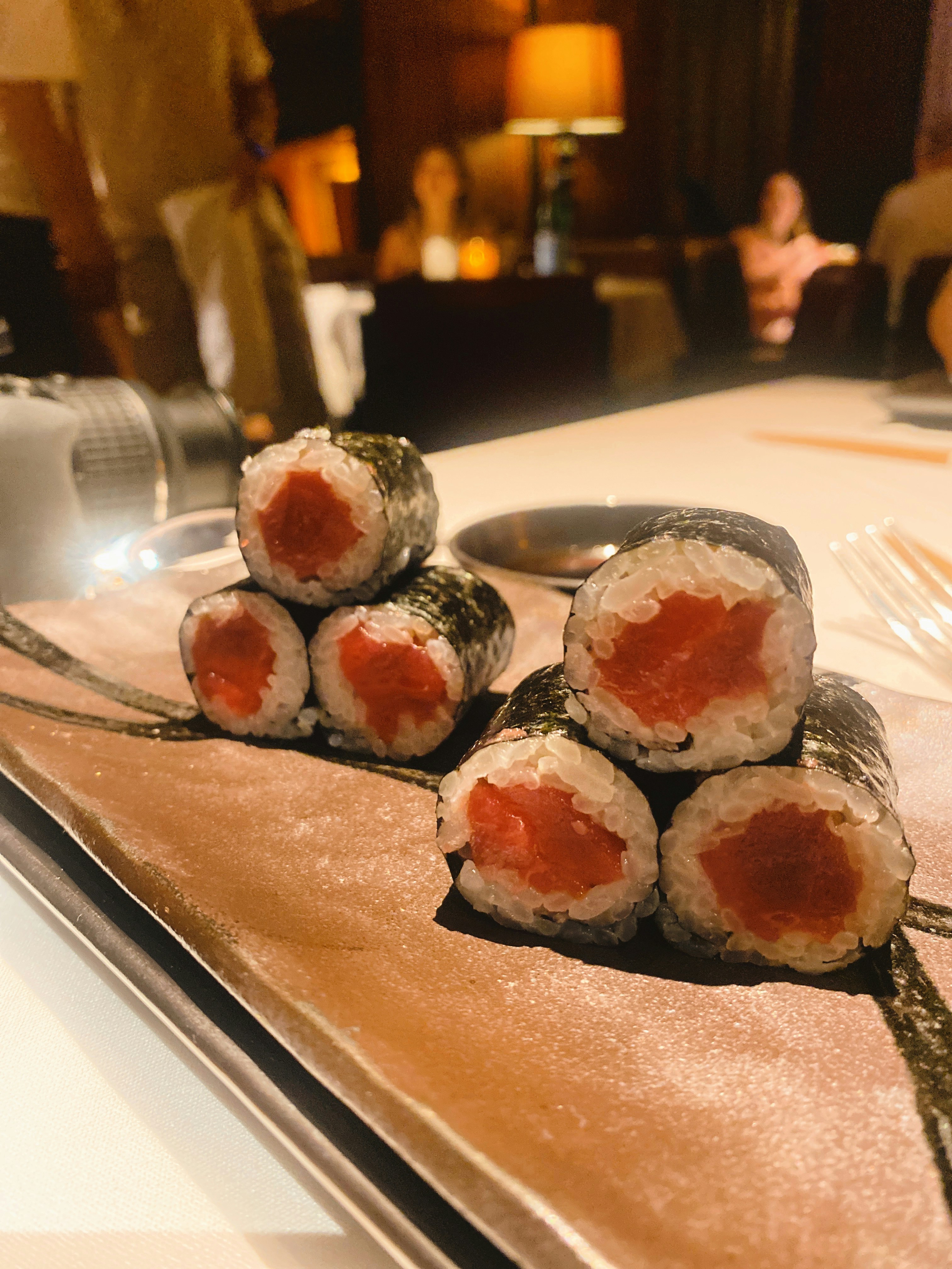 Fresh sushi rolls on dark slate plate, dim restaurant ambiance, deep shadows