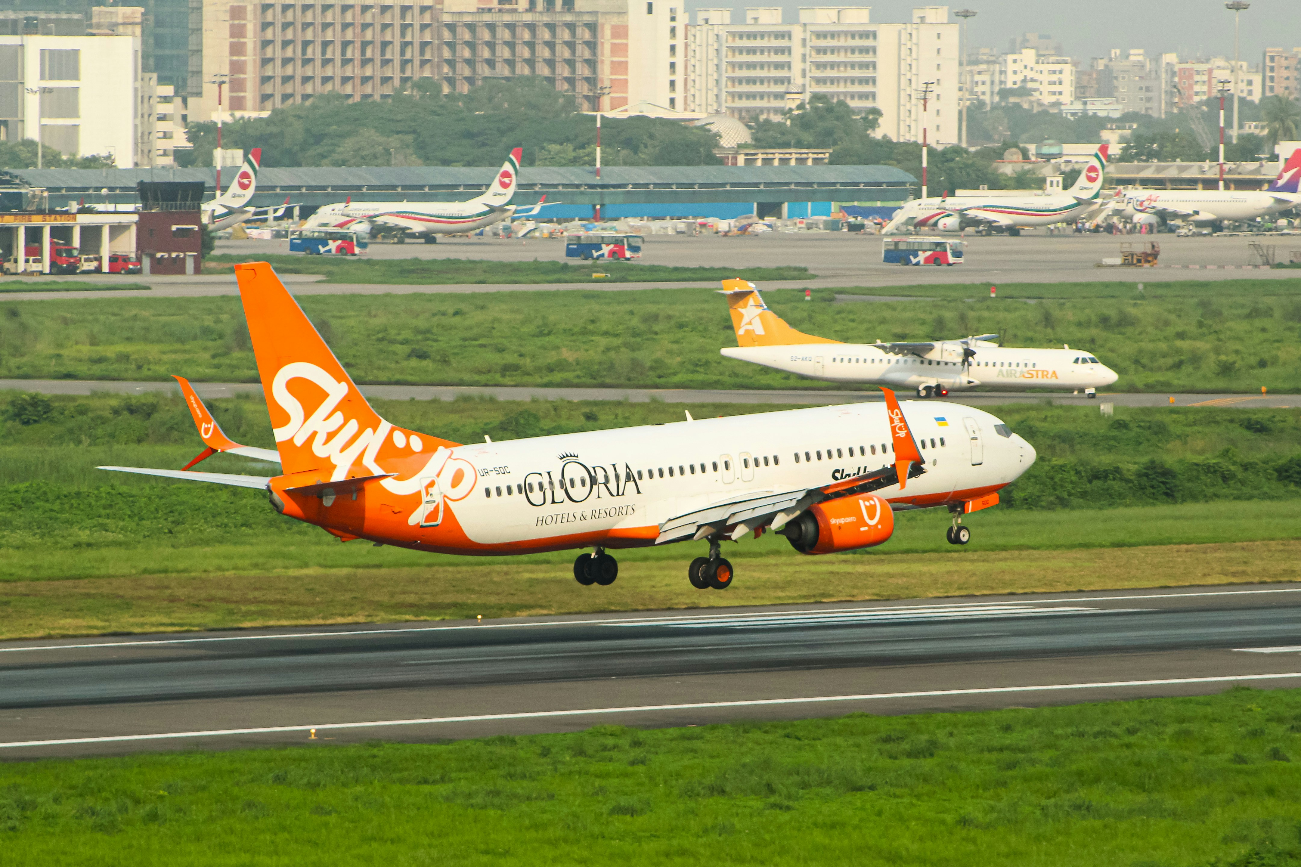 An orange and white jet airliner taking off from an airport runway, SkyUp Airlines operated by Us Bangla Airlines Boeing 737-800 Reg: UR-SQC