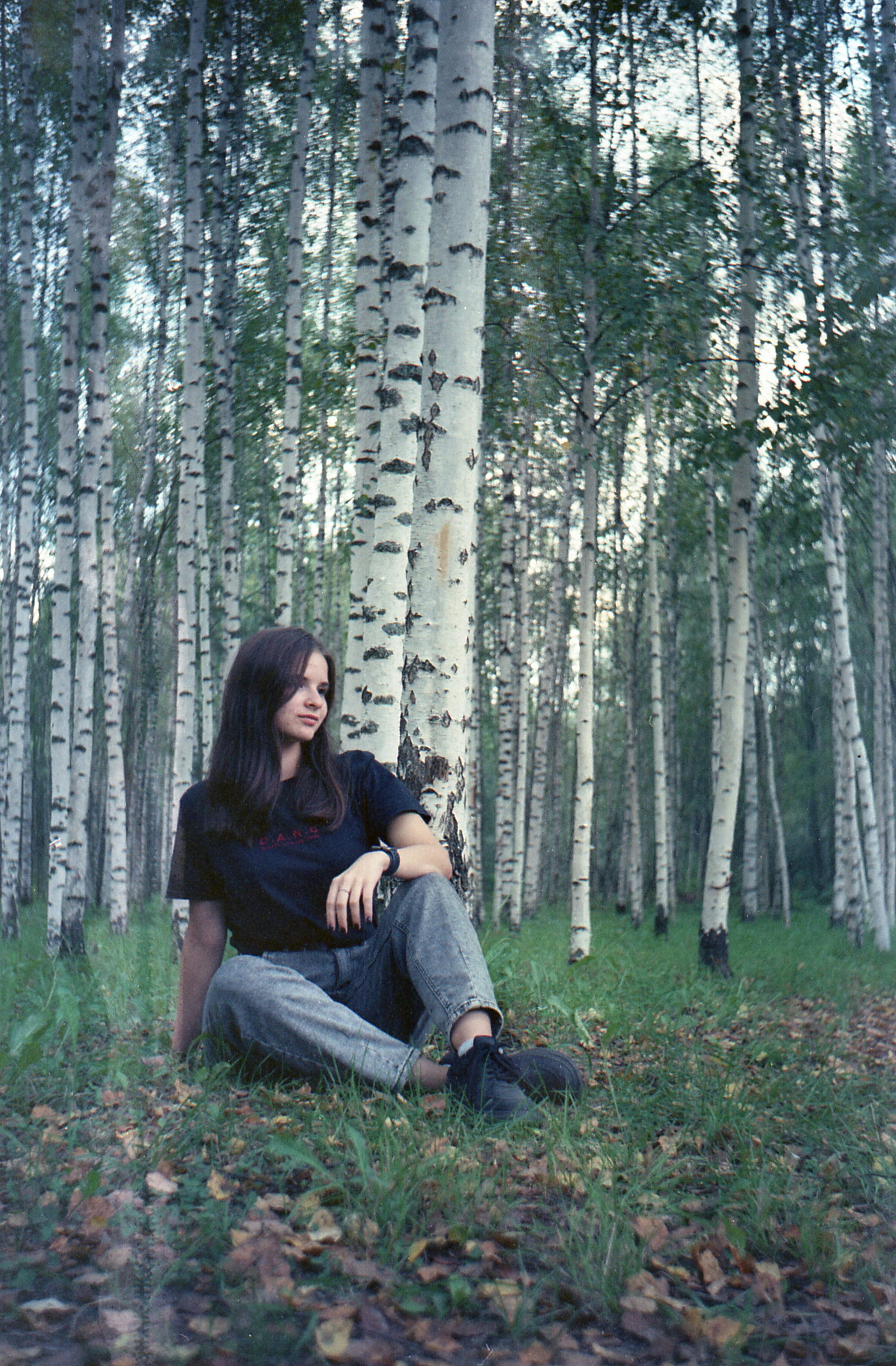 A woman sitting in the grass in front of a grove of trees
