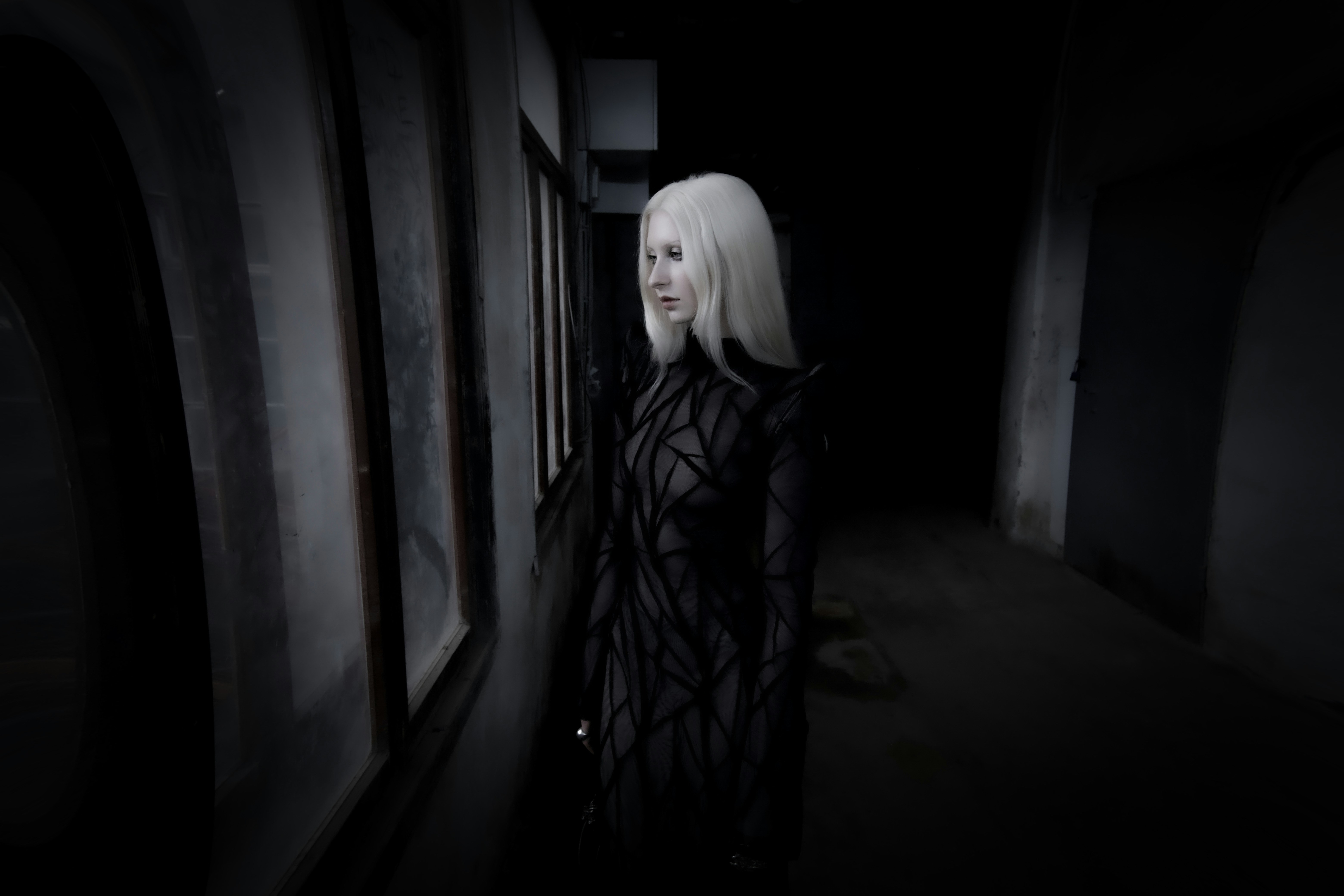 A woman standing in a dark hallway next to a window