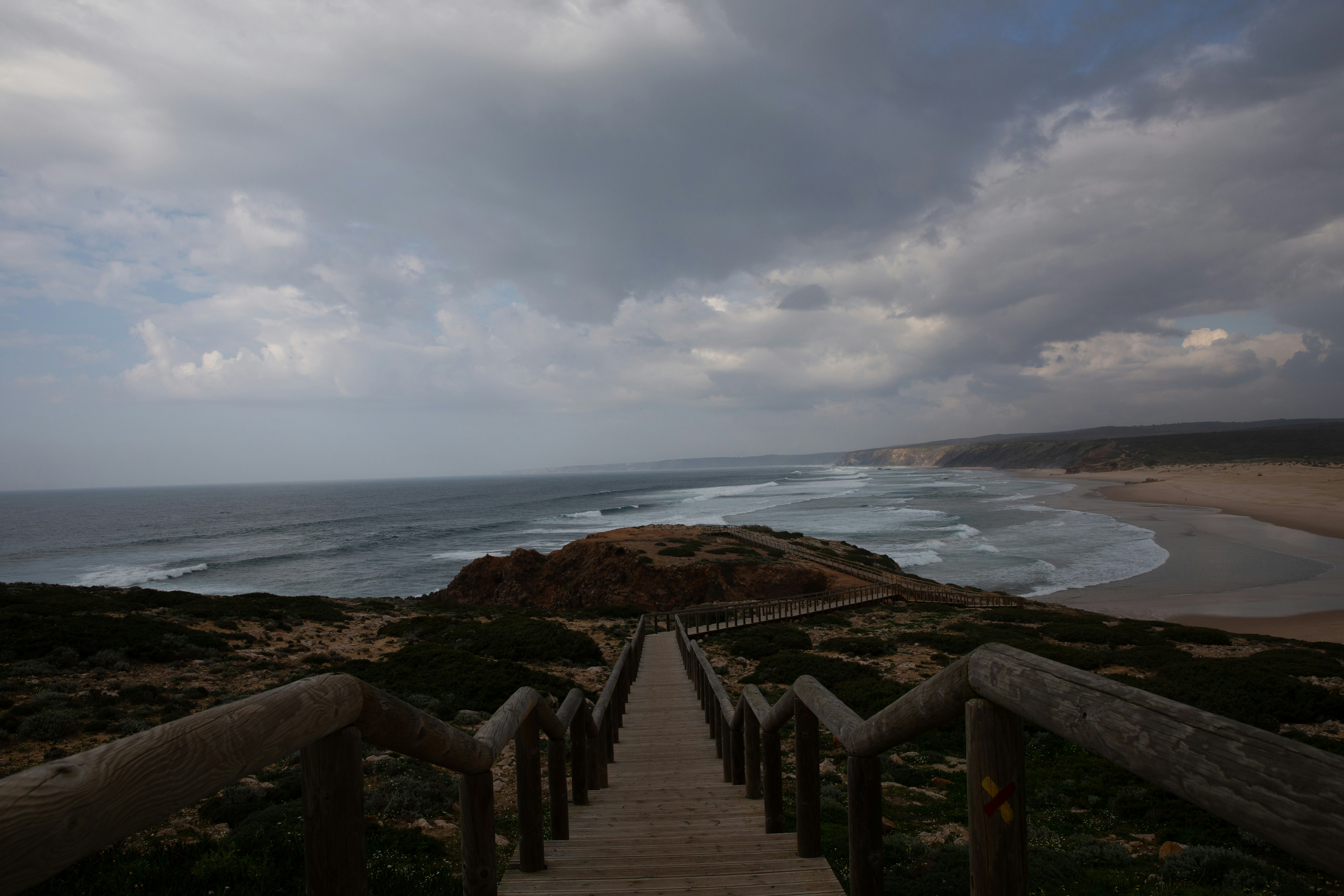 A wooden walkway leading to the beach under a cloudy sky