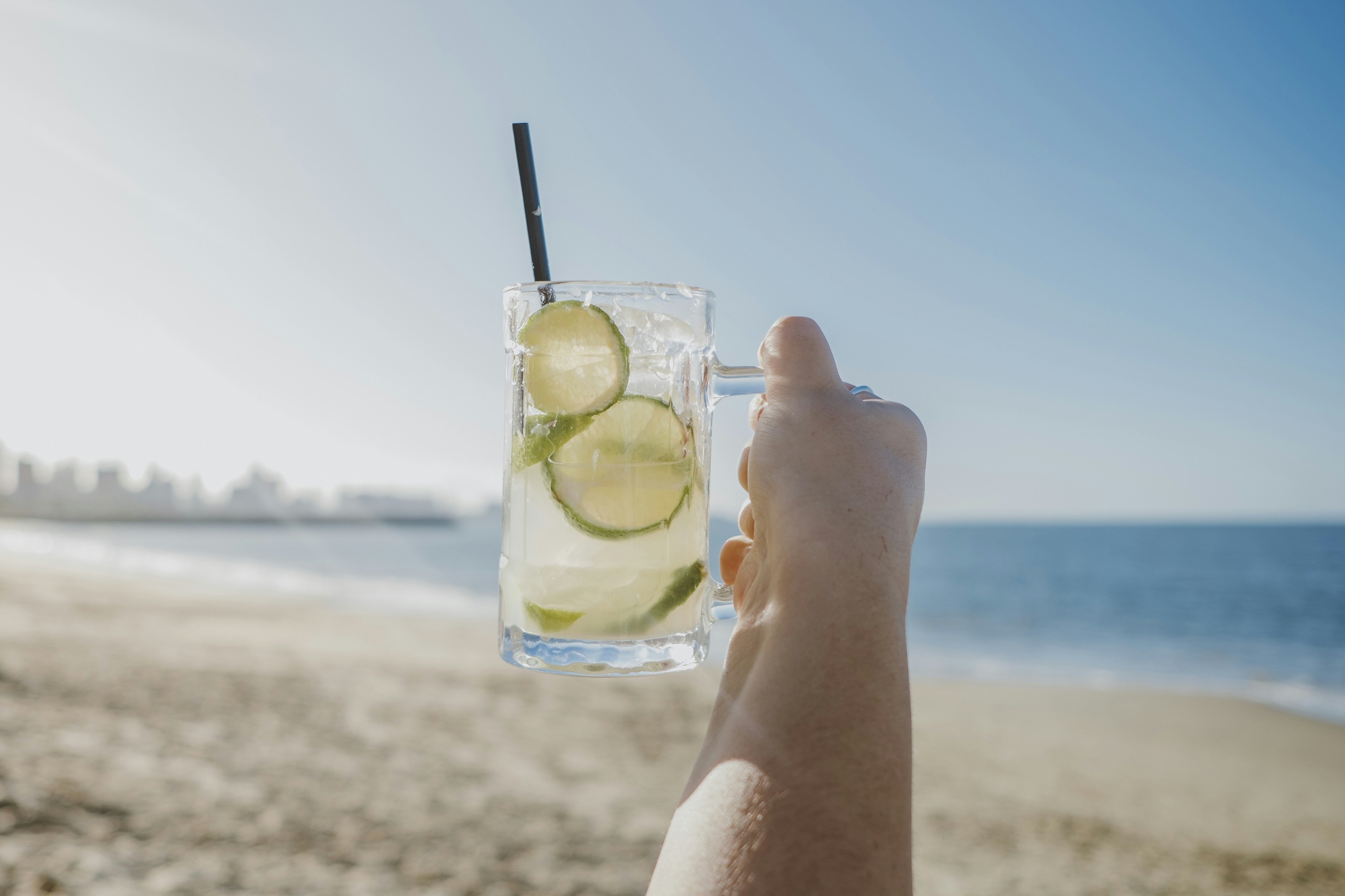 A person holding up a drink on the beach