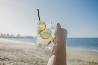 A person holding up a drink on the beach