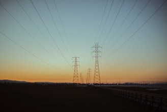 The sun is setting behind power lines in a field