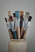 A white vase filled with lots of paint brushes