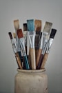 A white vase filled with lots of paint brushes