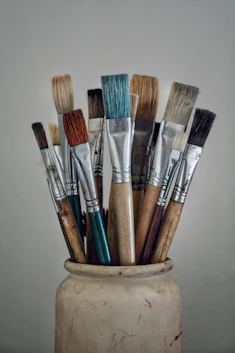 A white vase filled with lots of paint brushes