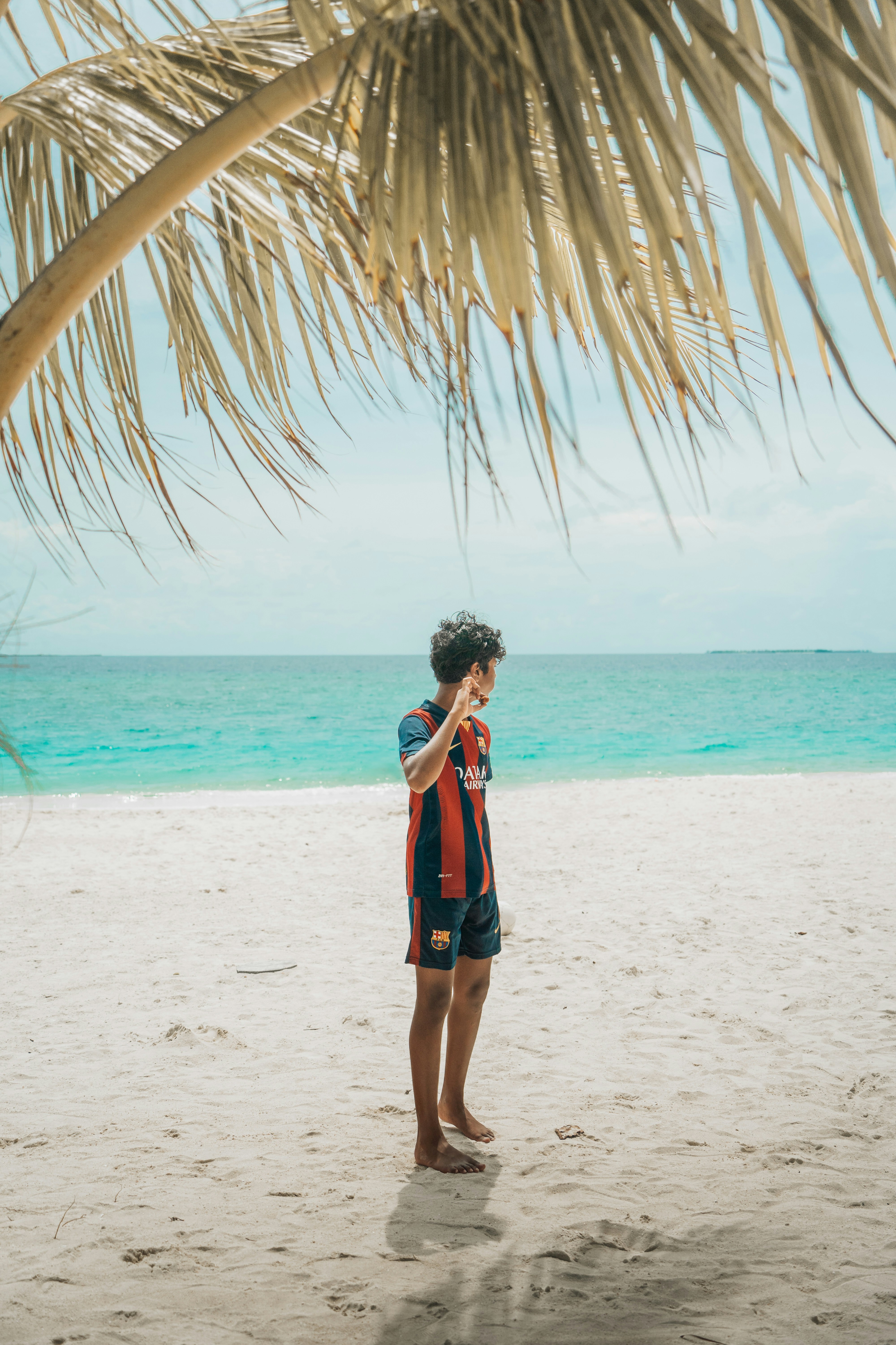 A man standing under a palm tree on a beach