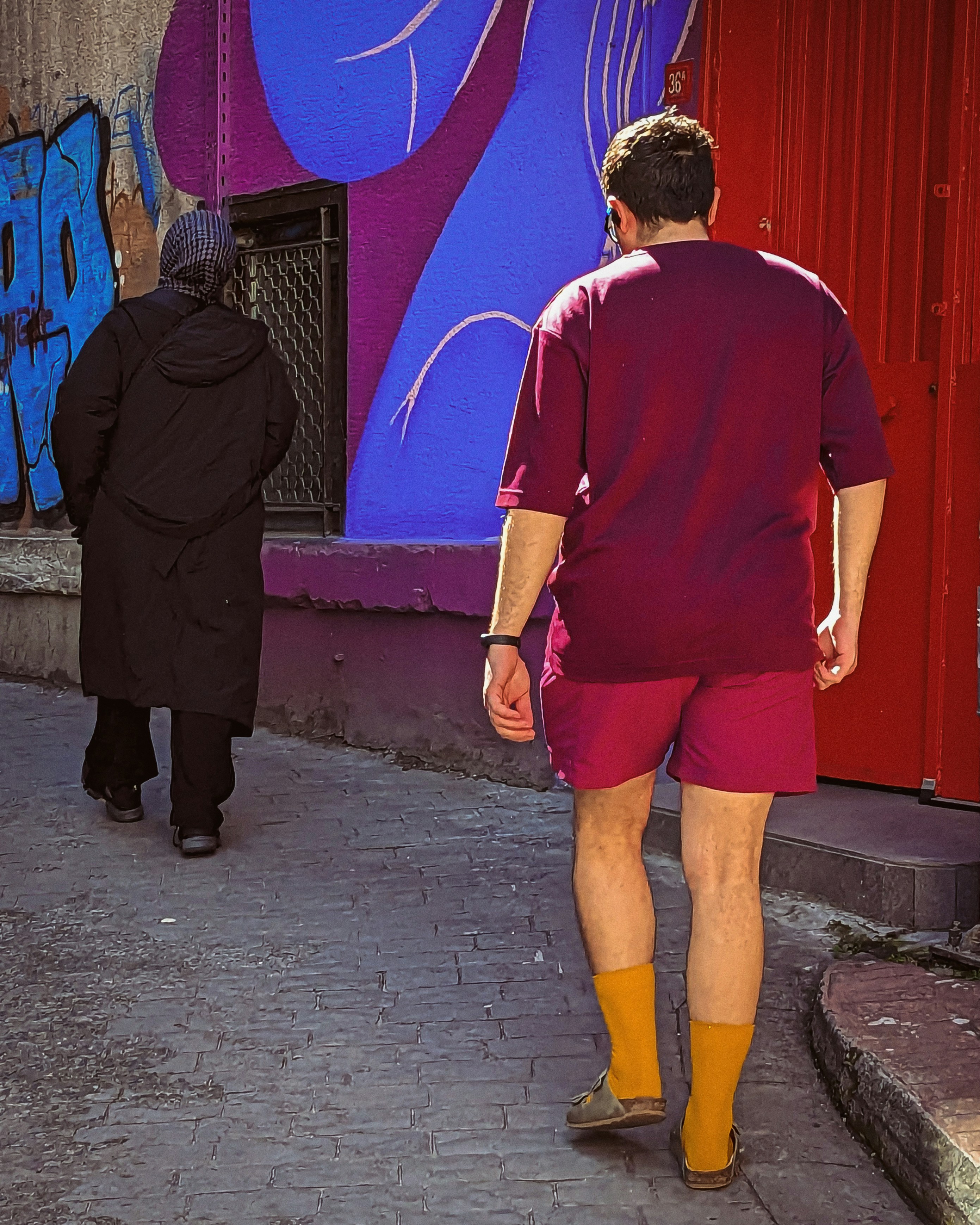 Un hombre caminando por una calle pasando por un edificio cubierto de grafitis