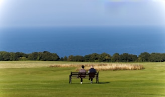 Two people sitting on a bench in a field