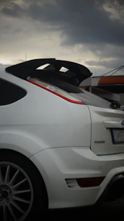 A white car parked in a parking lot under a cloudy sky