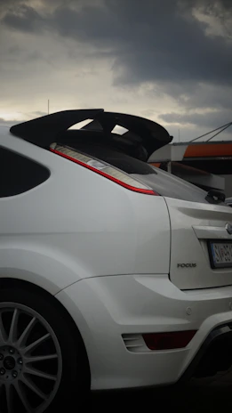 A white car parked in a parking lot under a cloudy sky