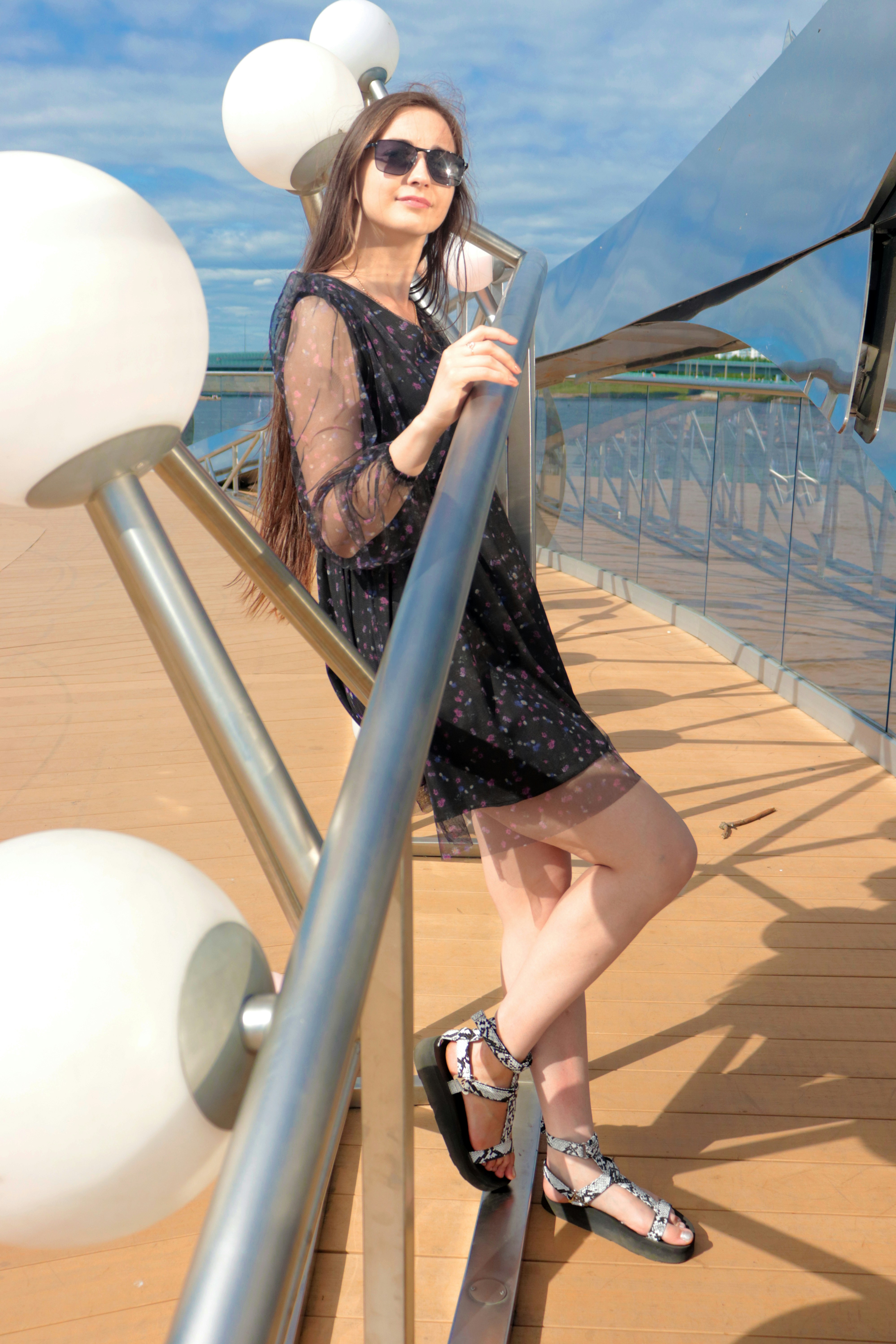 Una mujer con un vestido negro apoyada en un poste de metal