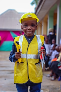 A young boy wearing a safety vest and holding a tool