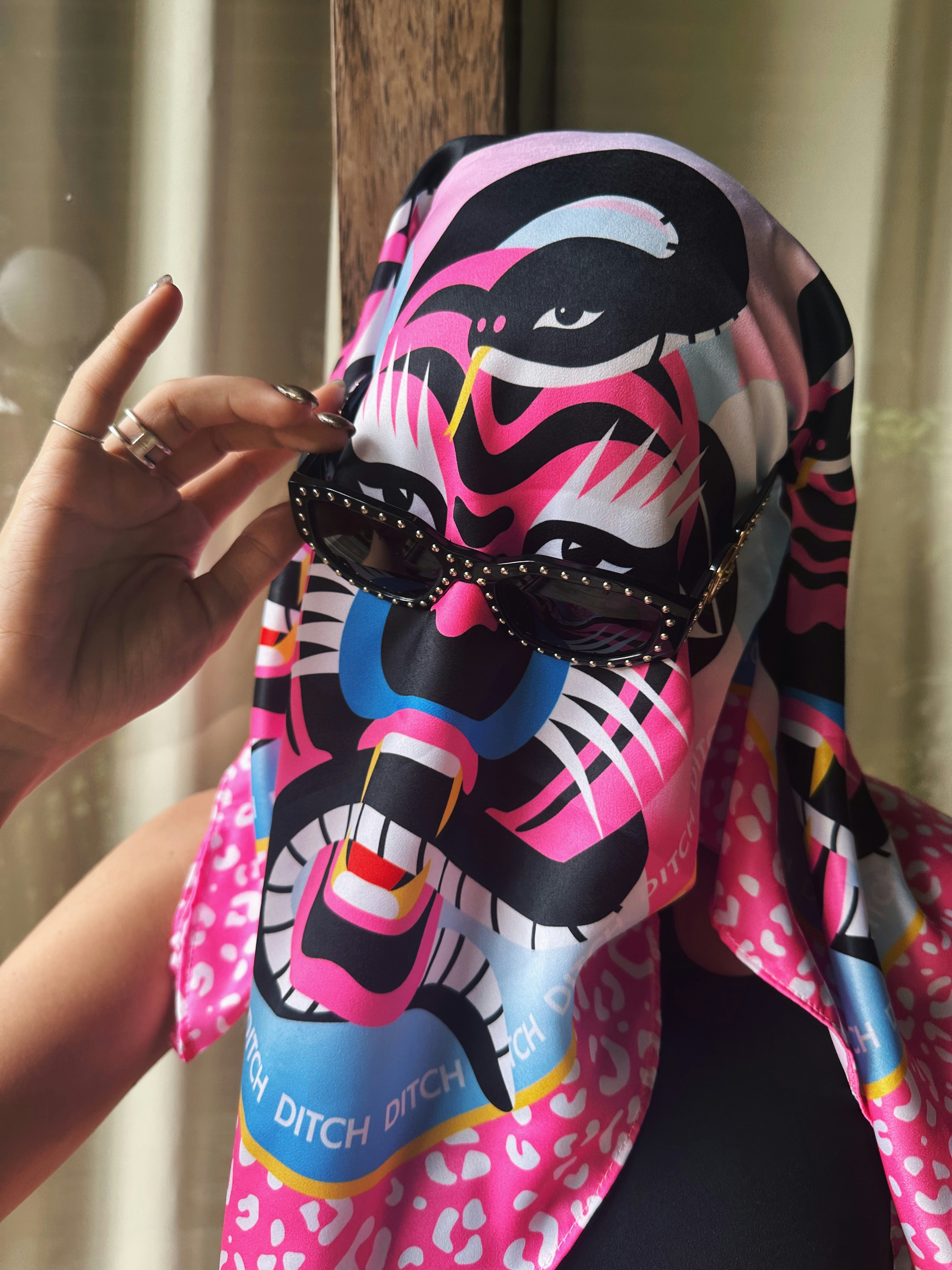 A woman wearing a colorful mask with her hand up to her face