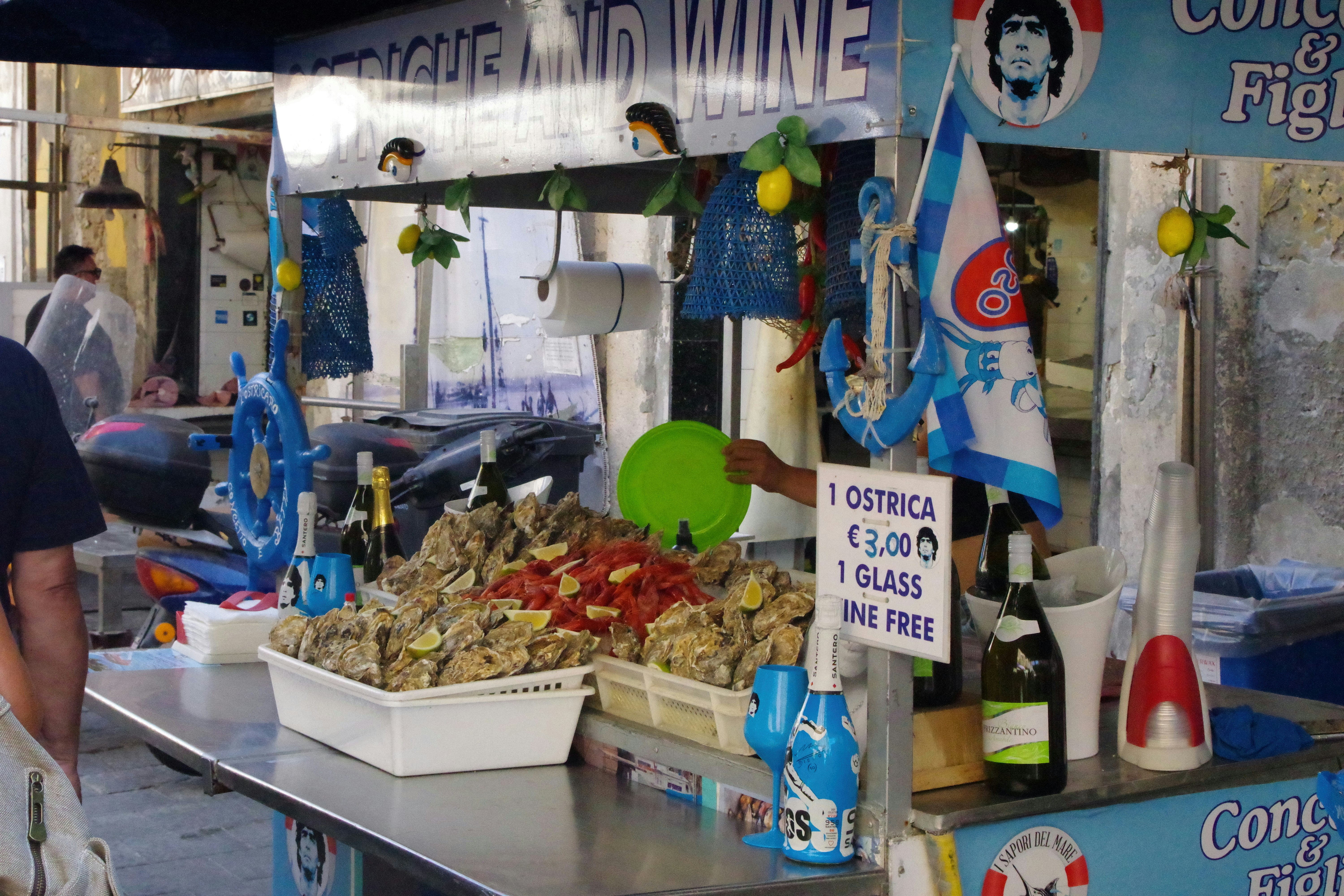 Street food stall selling oysters and shrimp with wine bottles.
