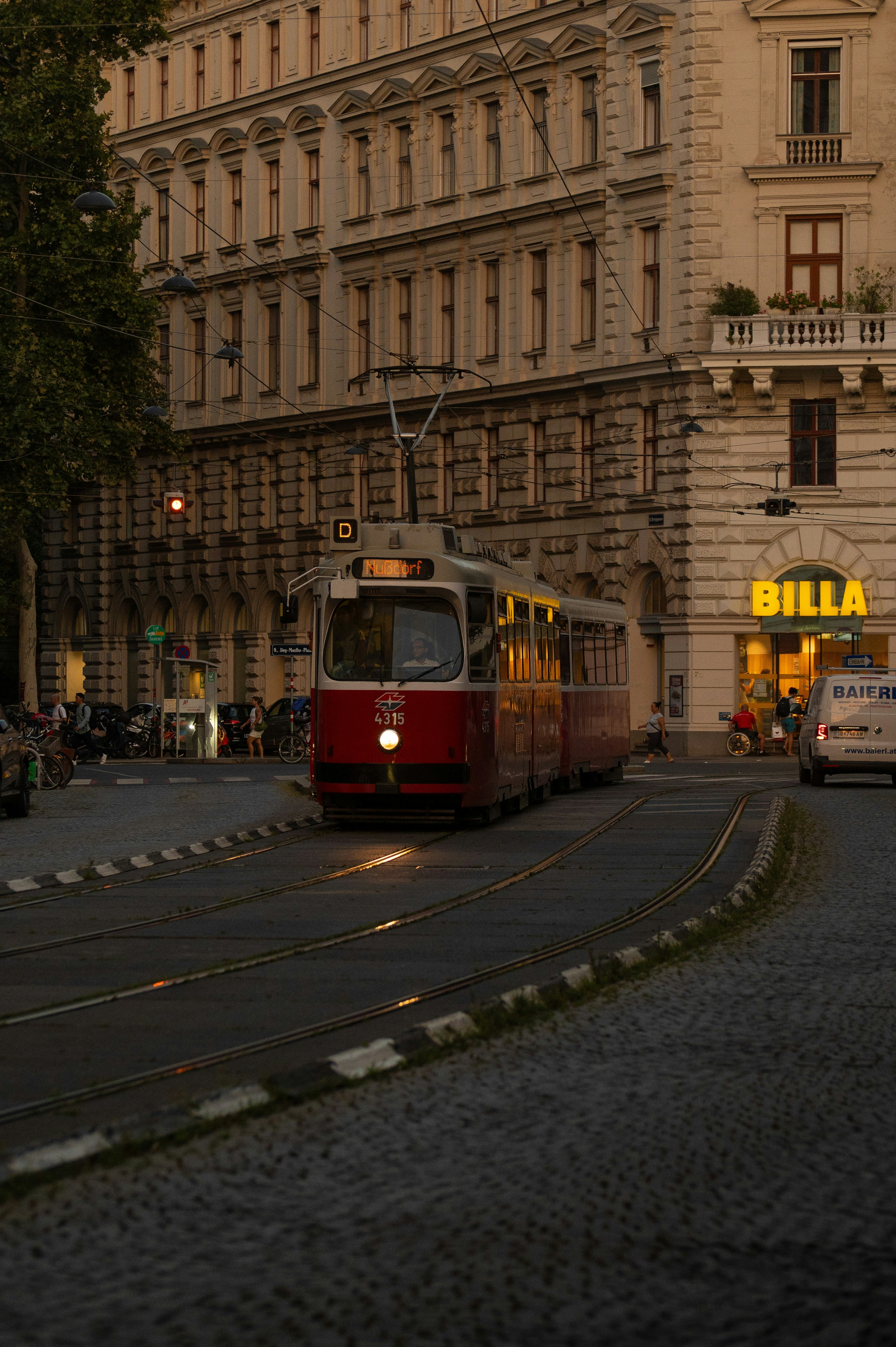 A red and white train traveling down a street next to a tall building
