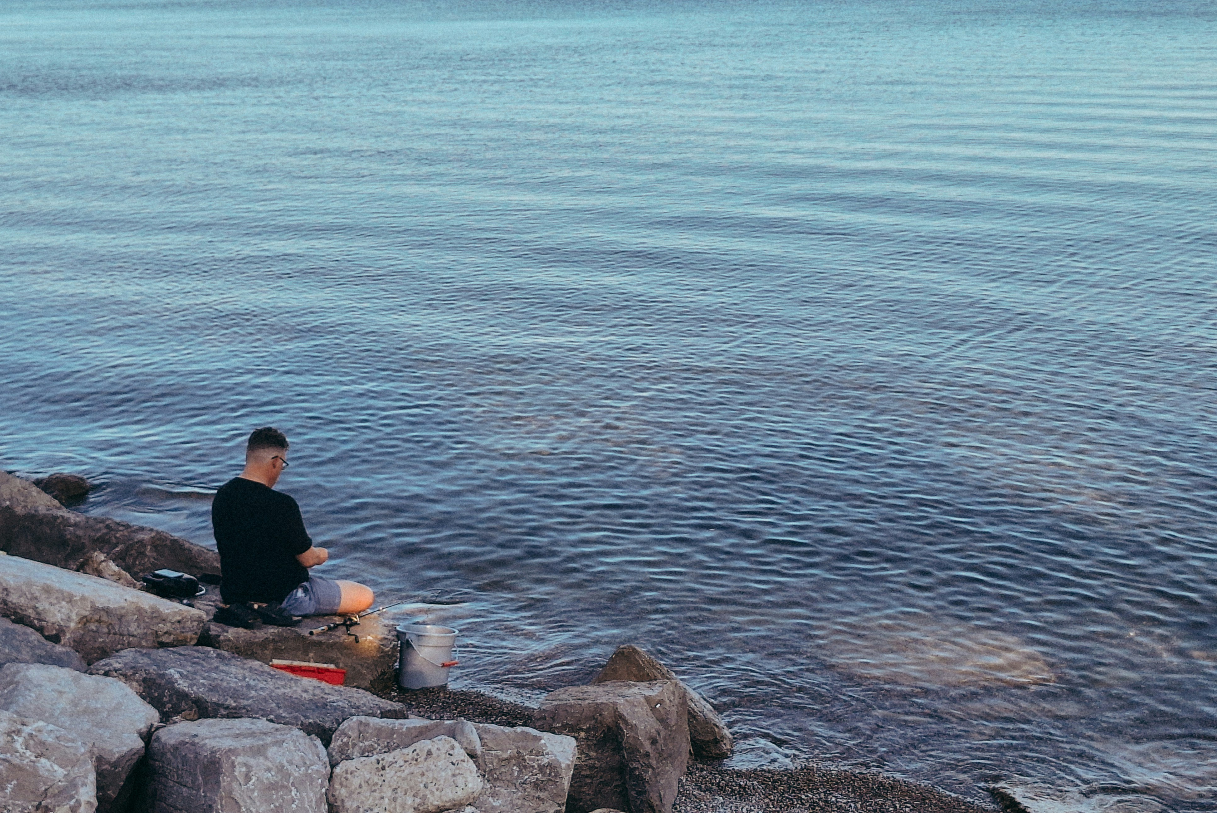 Ein Mann sitzt auf einem Felsen neben einem Gewässer