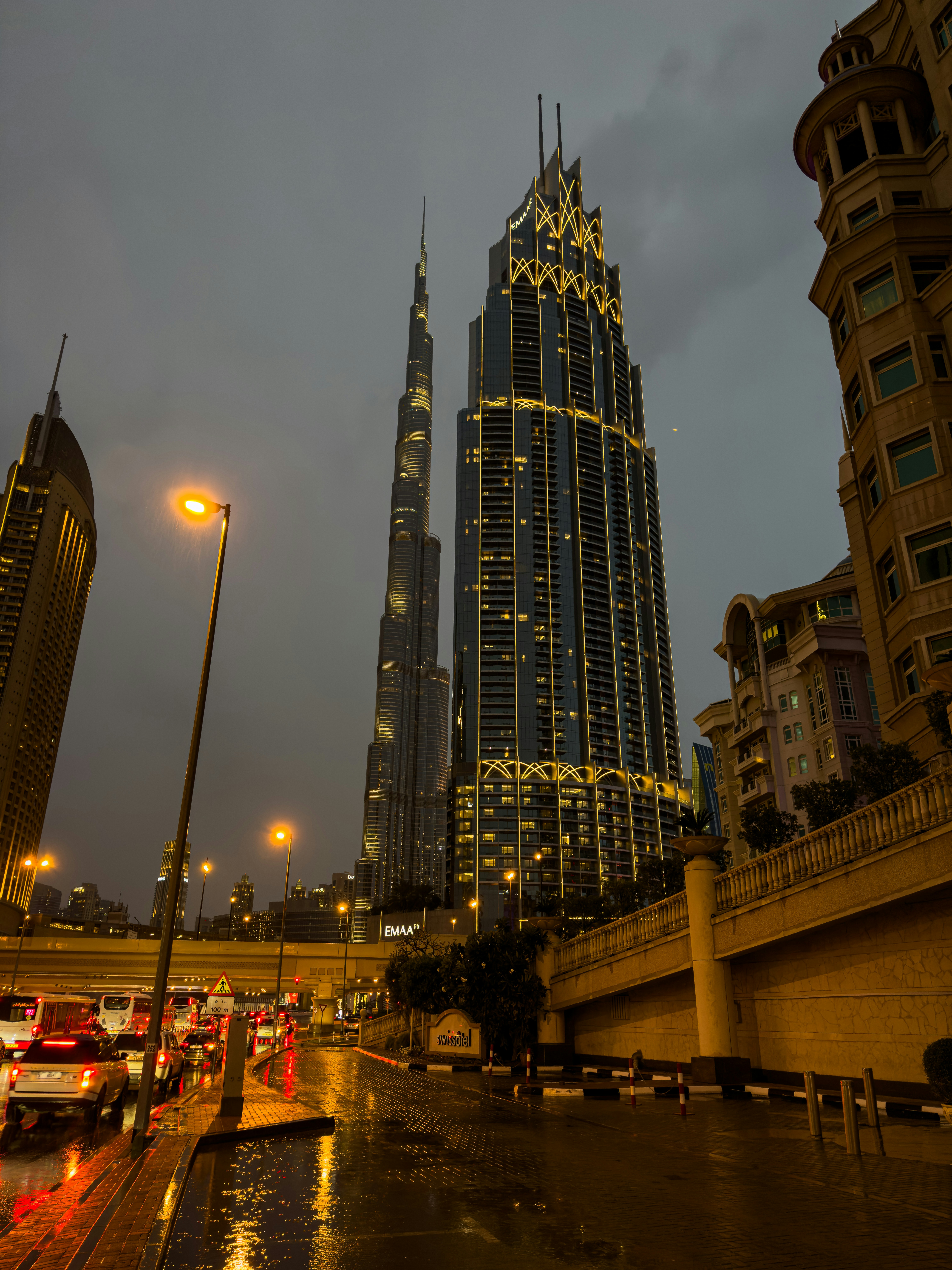 Dense city downtown at night, neon lights, skyscrapers, wet streets reflecting city glow, deep shadows between buildings
