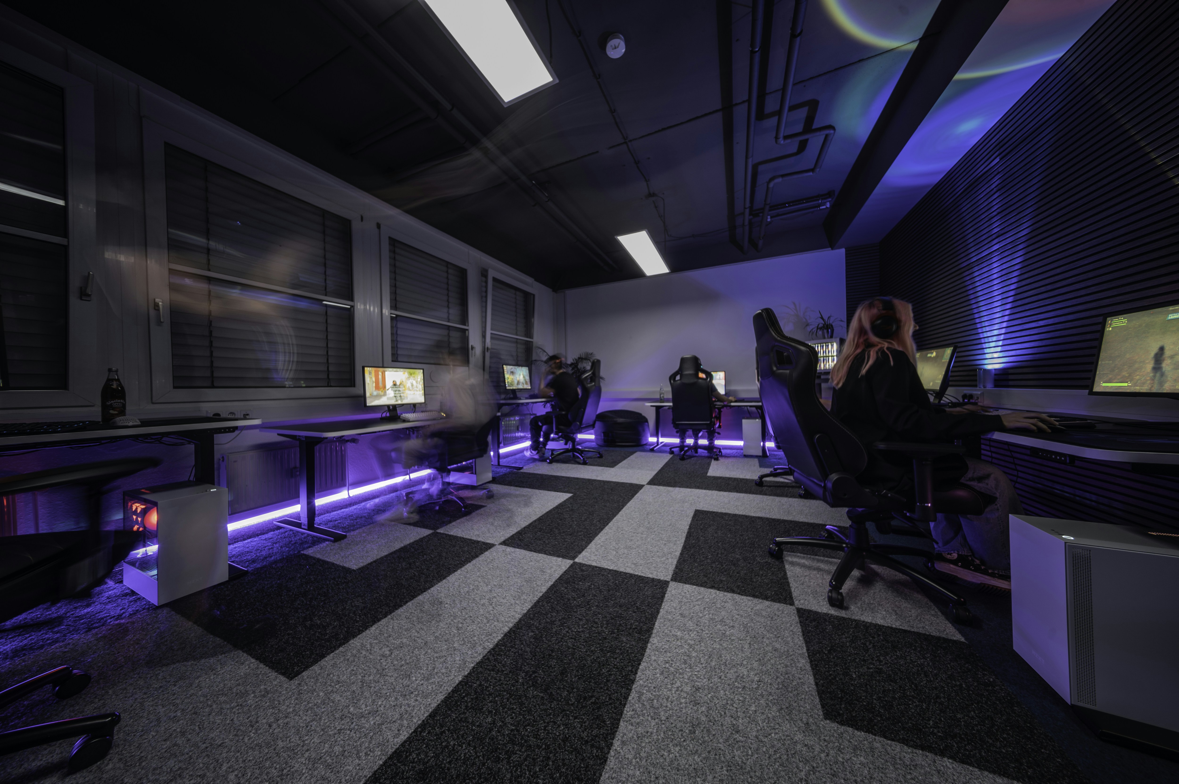 A group of people sitting in a room with a checkered floor, 1337Camp offers a unique environment perfectly tailored to the needs of gamers and creatives. Our facility features customizable lighting and LED floor lights that change colors to create the ideal atmosphere. The dojo-like design of the camp promotes a balance of relaxation and focus, allowing you to actively unwind while staying driven towards your goals. At 1337Camp, technology and design come together to create an inspiring and productive space that empowers you to reach your full potential.