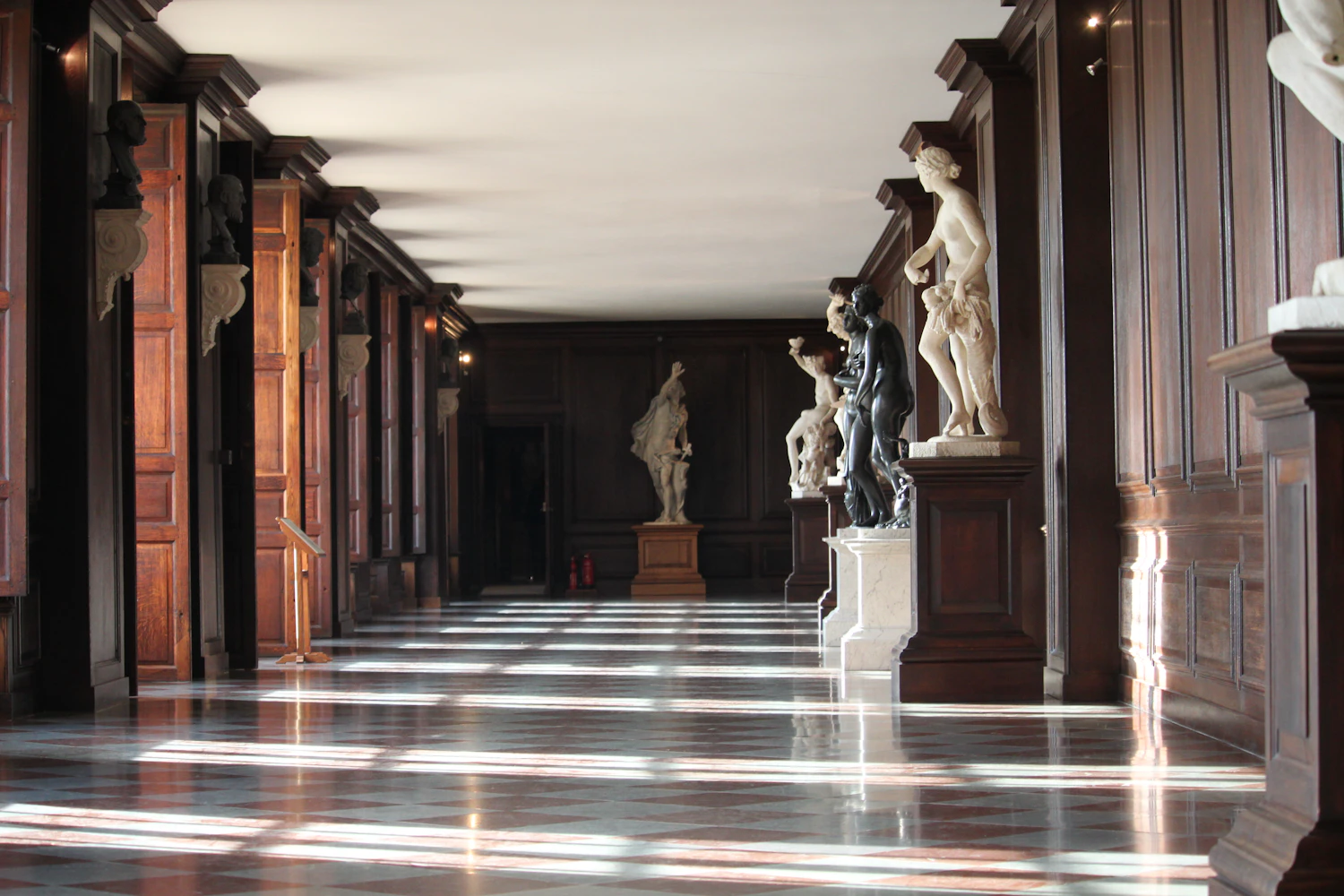 A corridor of standing figures in pale stone, raking light across the floor