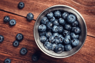 A metal bowl filled with blueberries on top of a wooden table