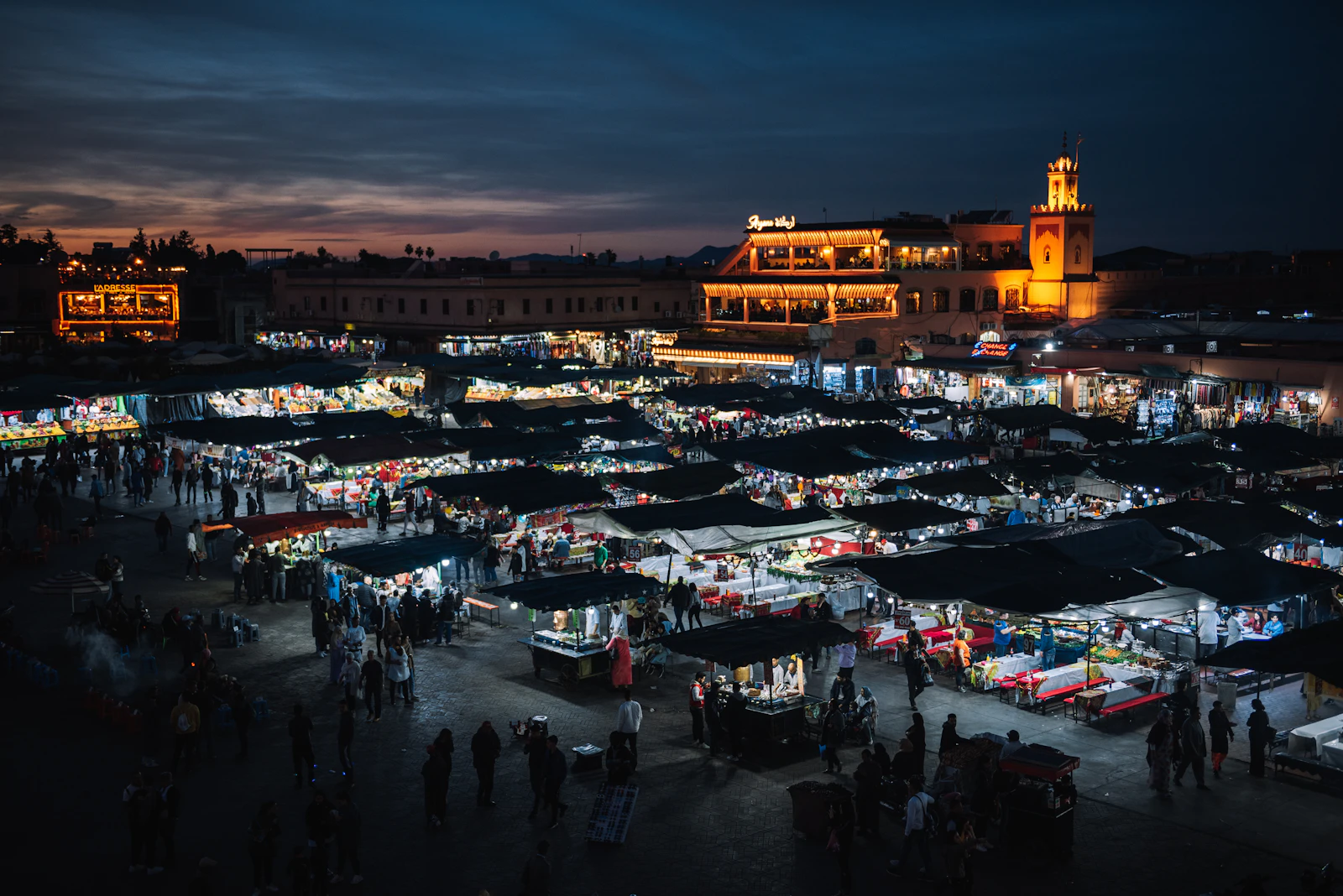 Rooftop view over Jemaa el-Fnaa in the Marrakech medina at dusk, lantern-lit stalls under a blue-hour sky