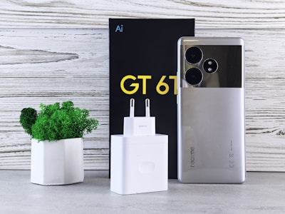 A cell phone sitting next to a box and a plant