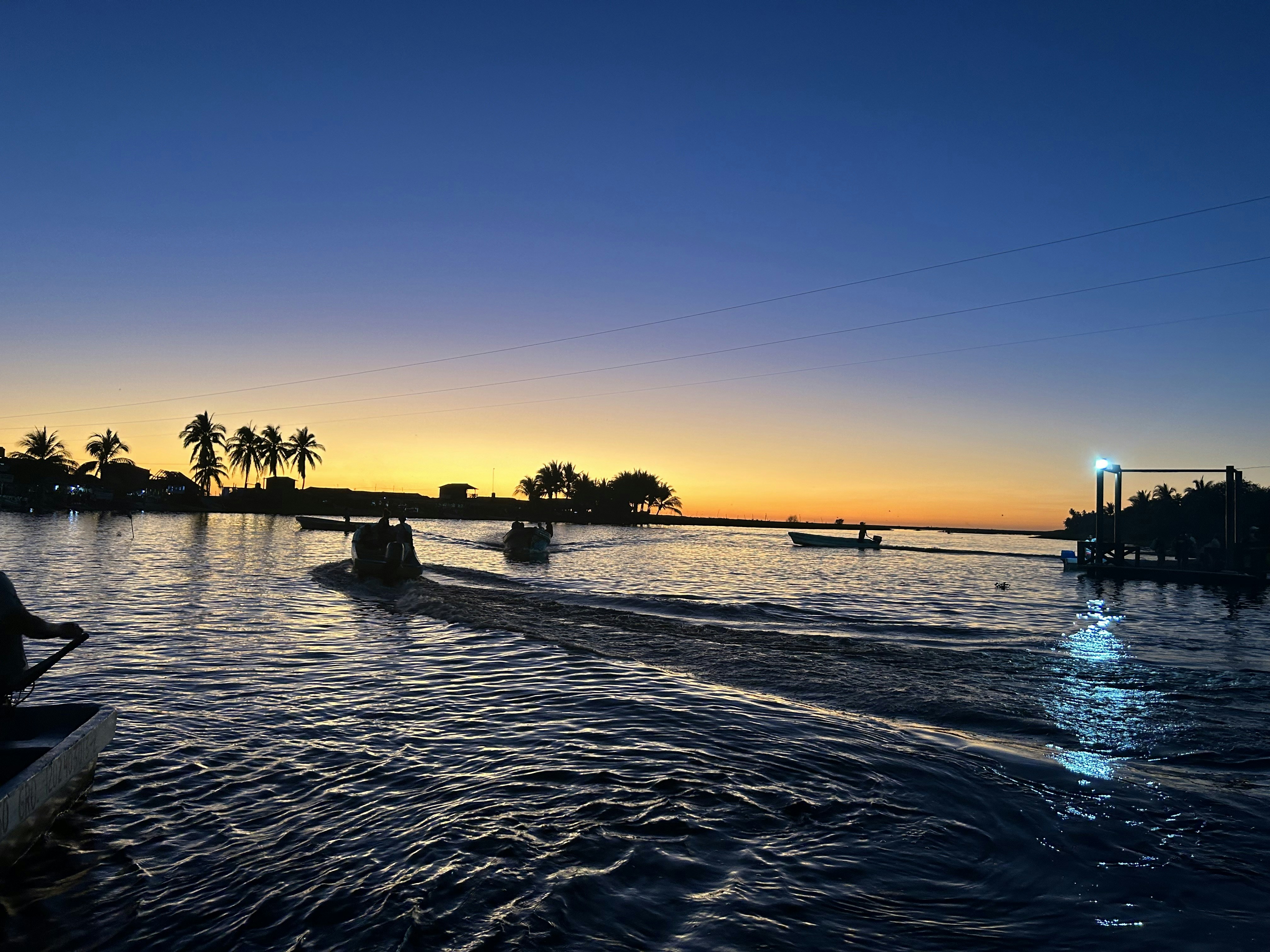 Luxury boat on calm golden ocean at sunset with silhouetted palm trees on horizon