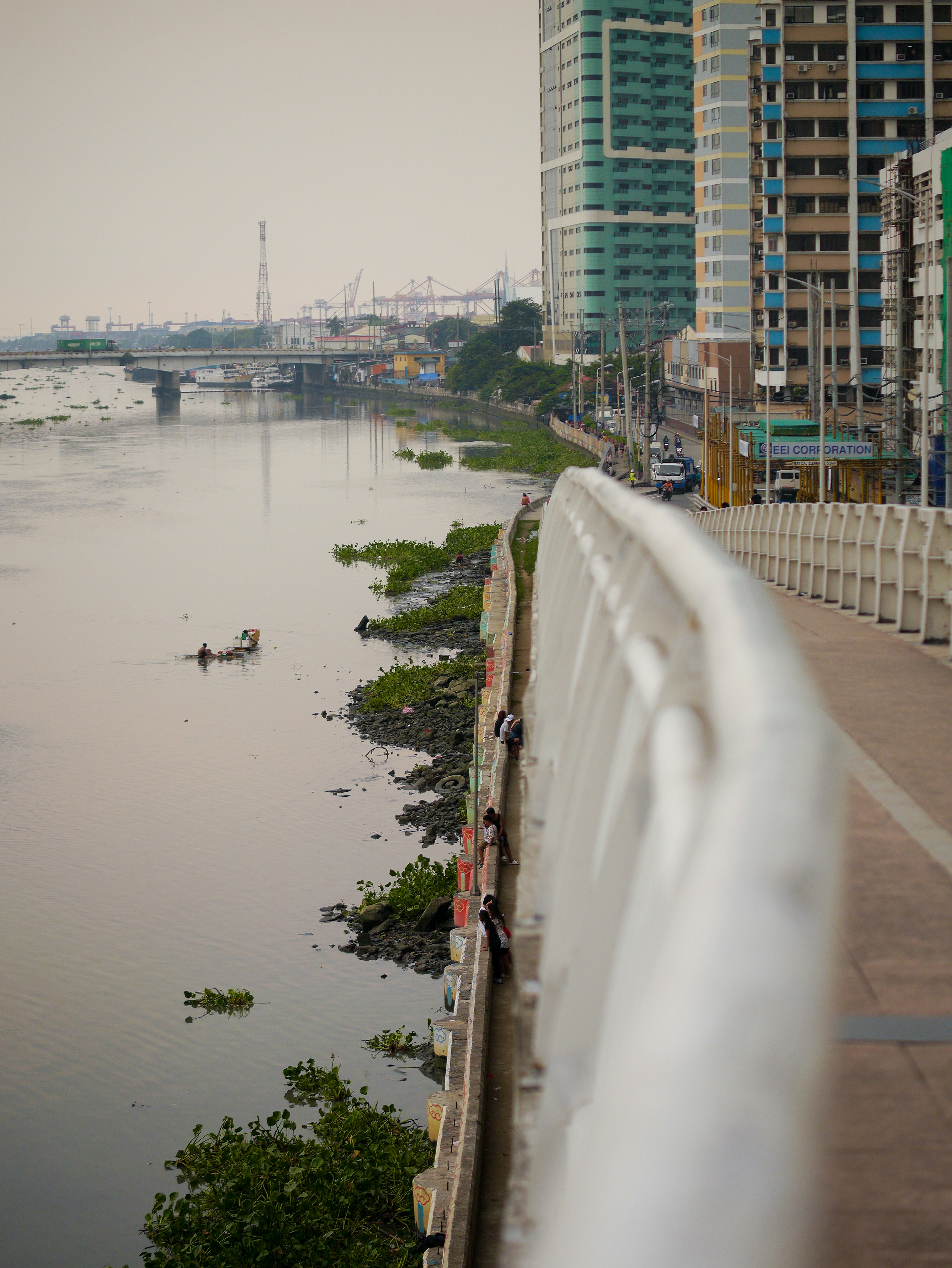 Un hombre montando una patineta por una acera junto a un cuerpo de agua