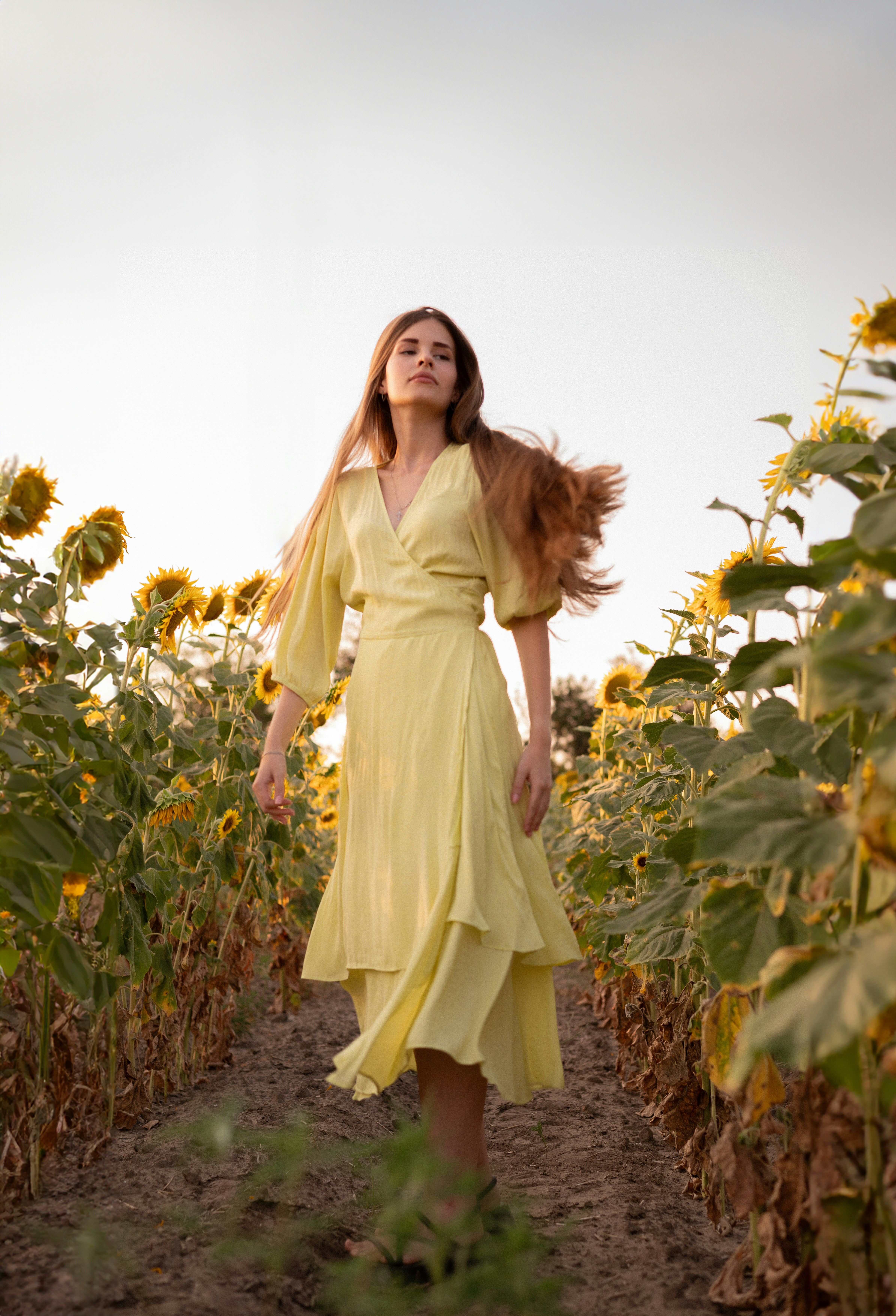 A woman in a yellow dress walking through a field of sunflowers