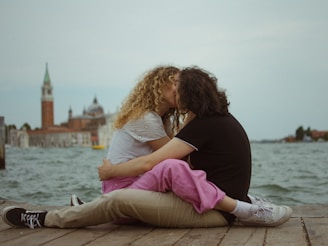 A man and a woman sitting on a pier kissing